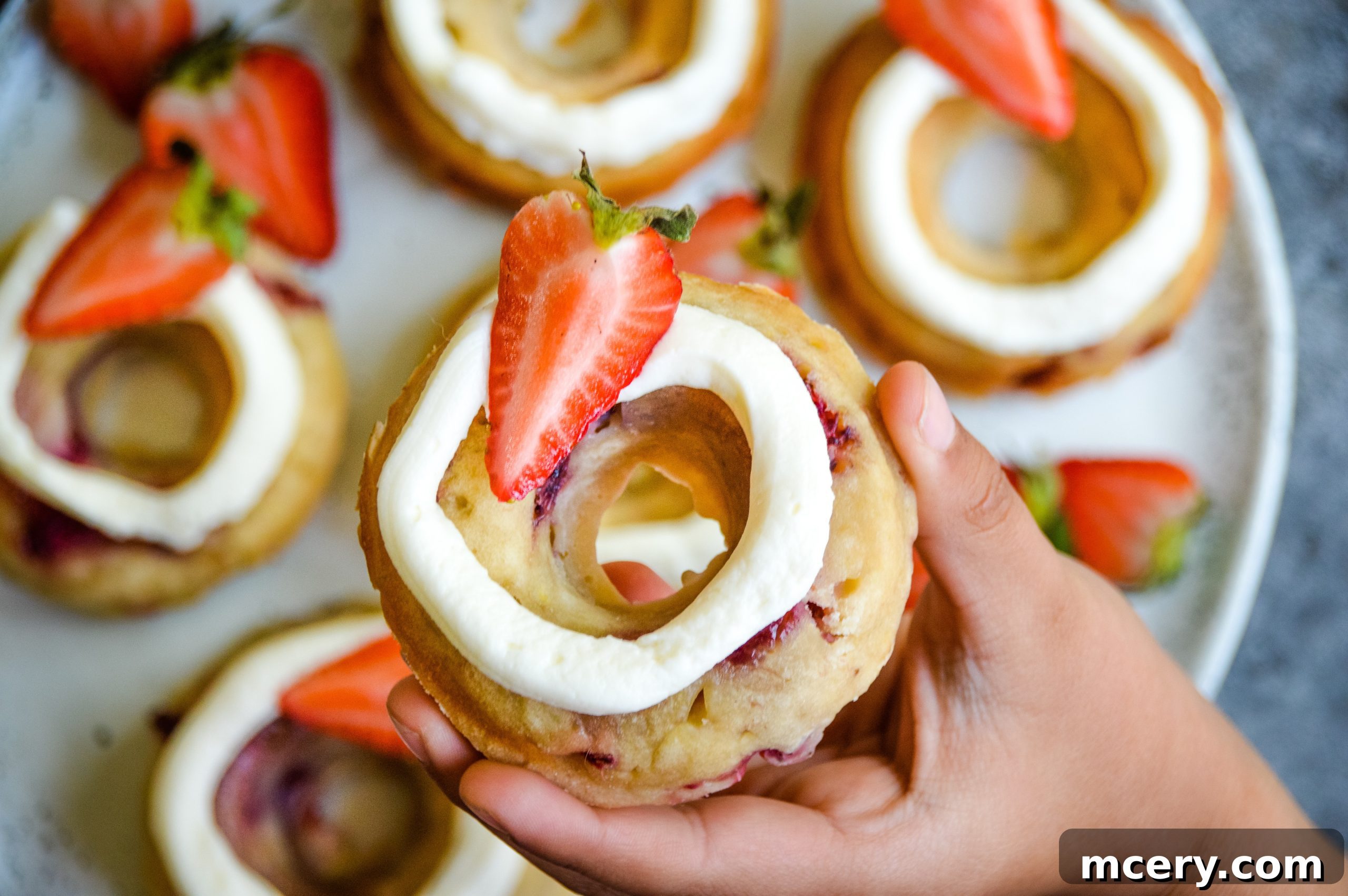 Irresistible Strawberry Banana Donuts 2 A close-up shot of several freshly baked Strawberry Banana Donuts on a wire cooling rack, topped with a creamy white frosting and garnished with fresh strawberry slices.