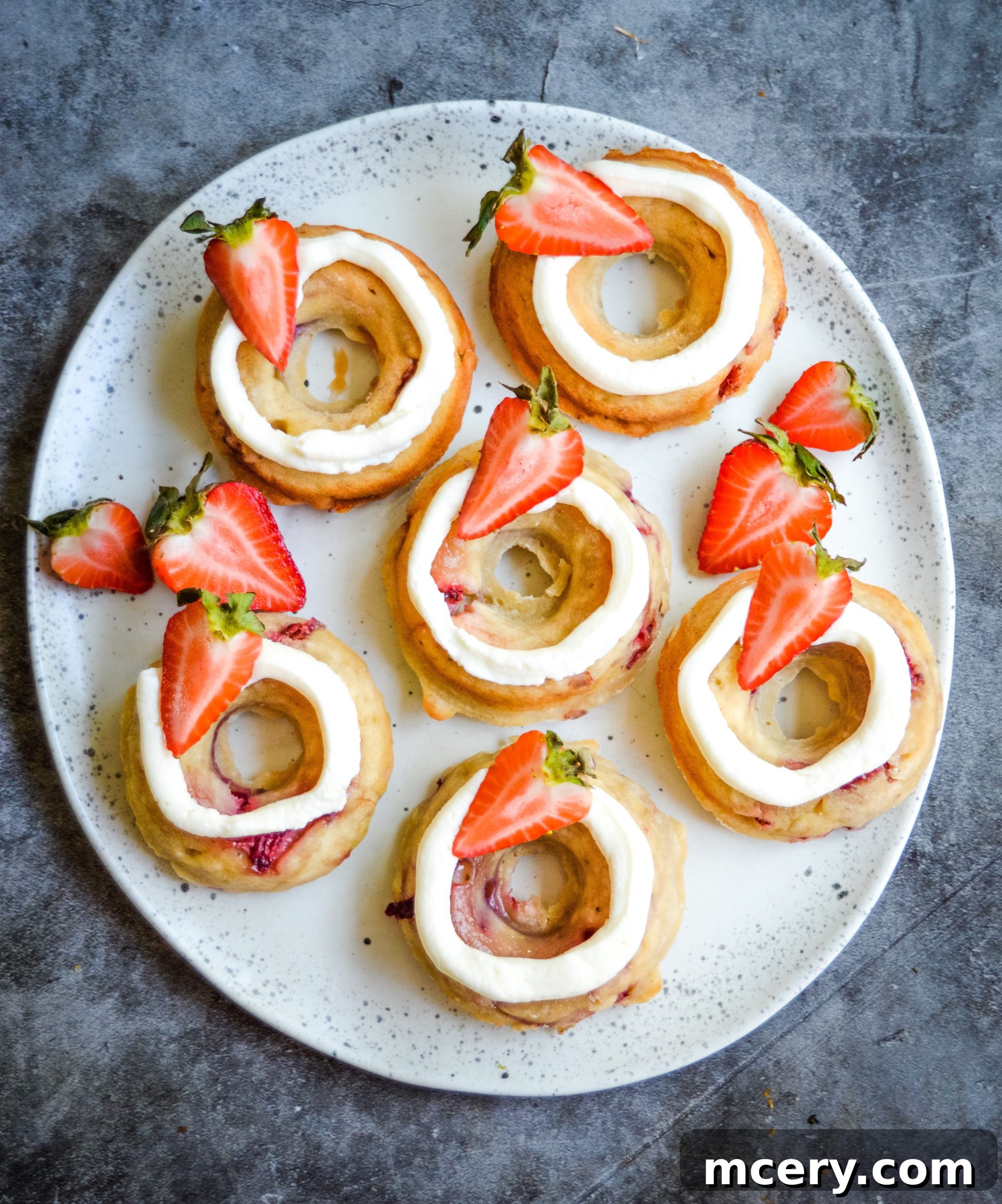 Irresistible Strawberry Banana Donuts 6 A stack of three Strawberry Banana Donuts, showing the layers of soft cake and creamy frosting, garnished with strawberry slices.