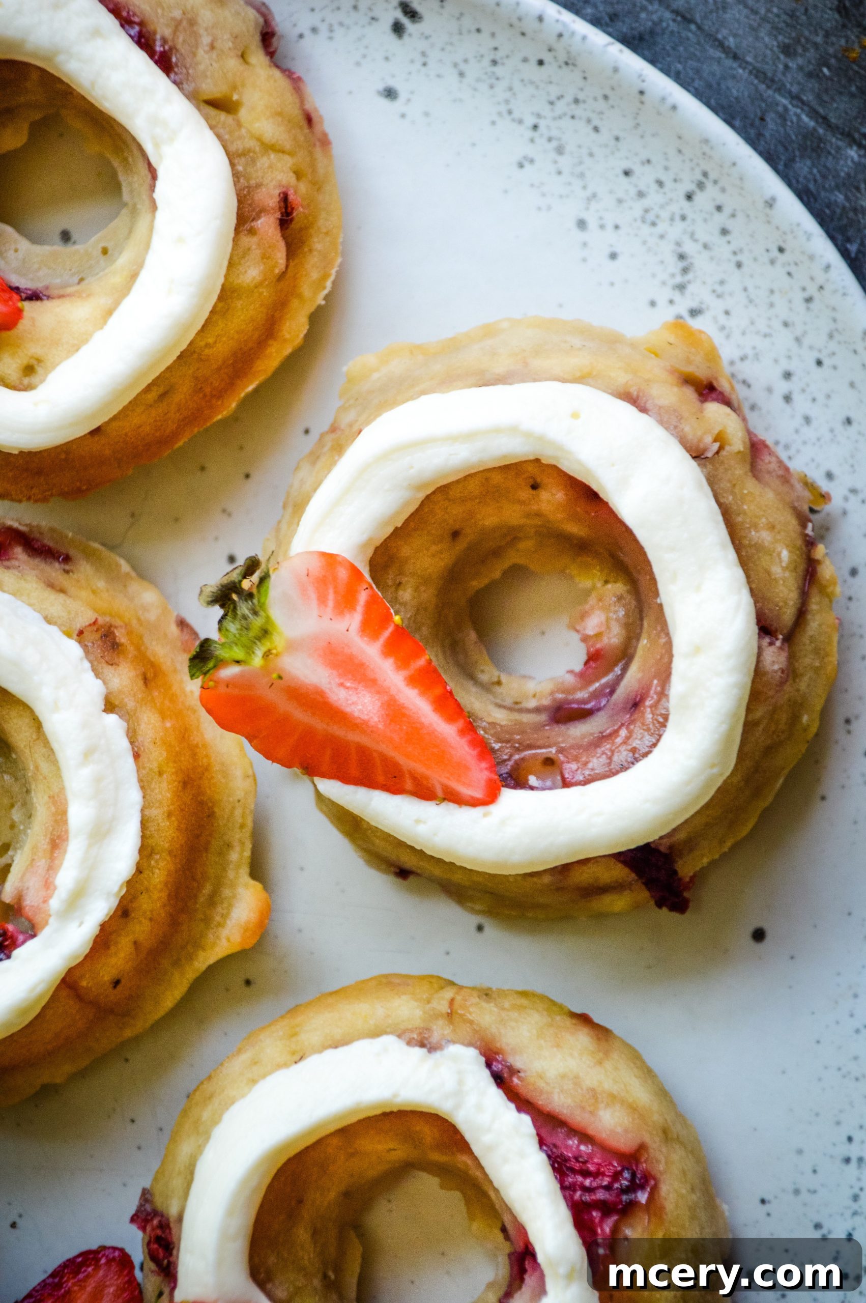 Irresistible Strawberry Banana Donuts 8 A close-up, top-down view of two frosted Strawberry Banana Donuts on a white plate, highlighting their appetizing appearance.