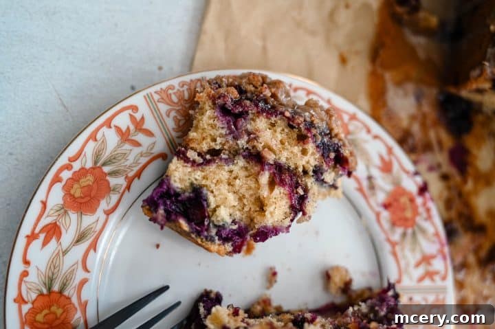 Moist Bakery Style Blueberry Burst Coffee Cake 15 A slice of blueberry coffee cake served with a mug of coffee and fresh blueberries.