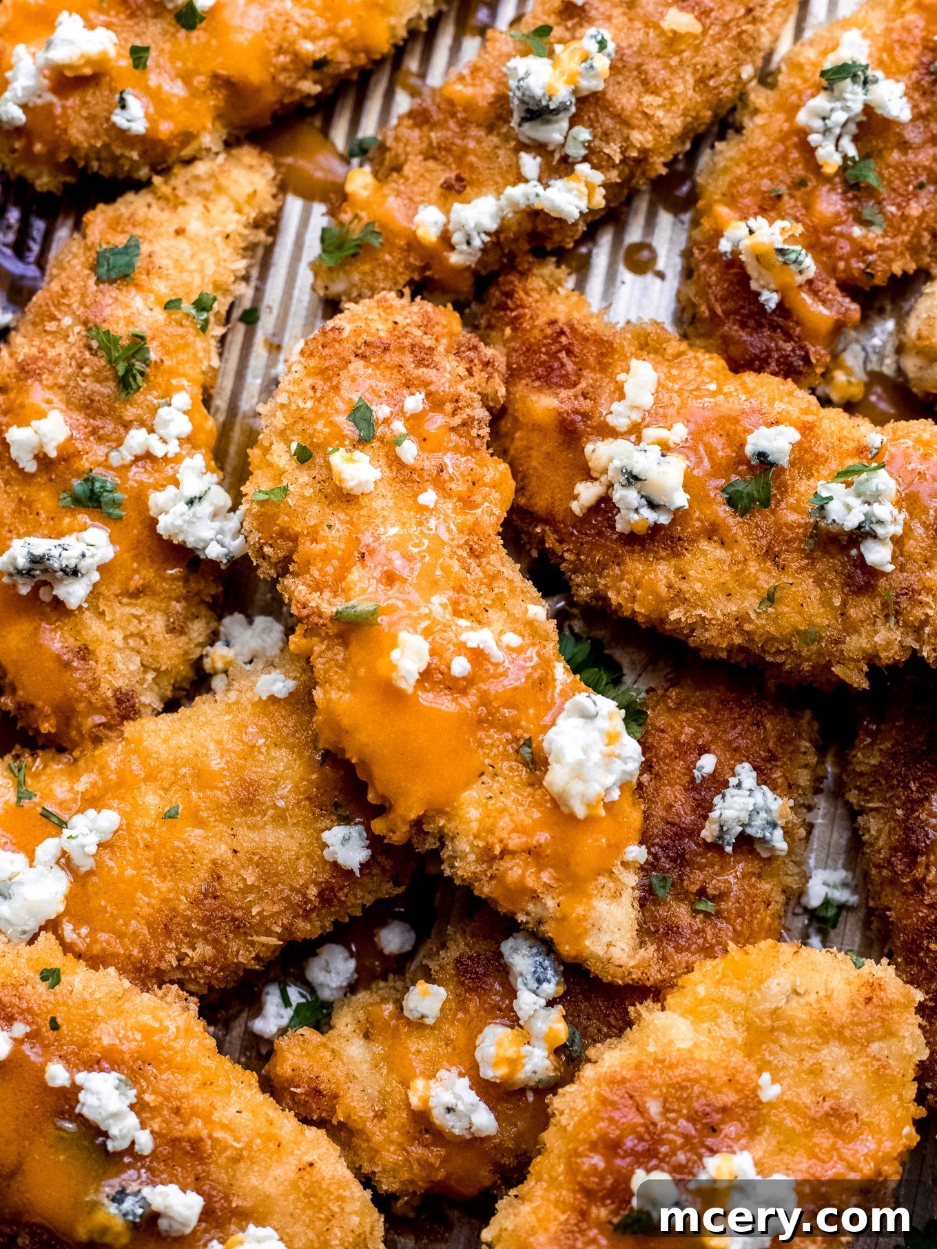 Stacked baked buffalo chicken tenders on a plate, garnished with fresh herbs.