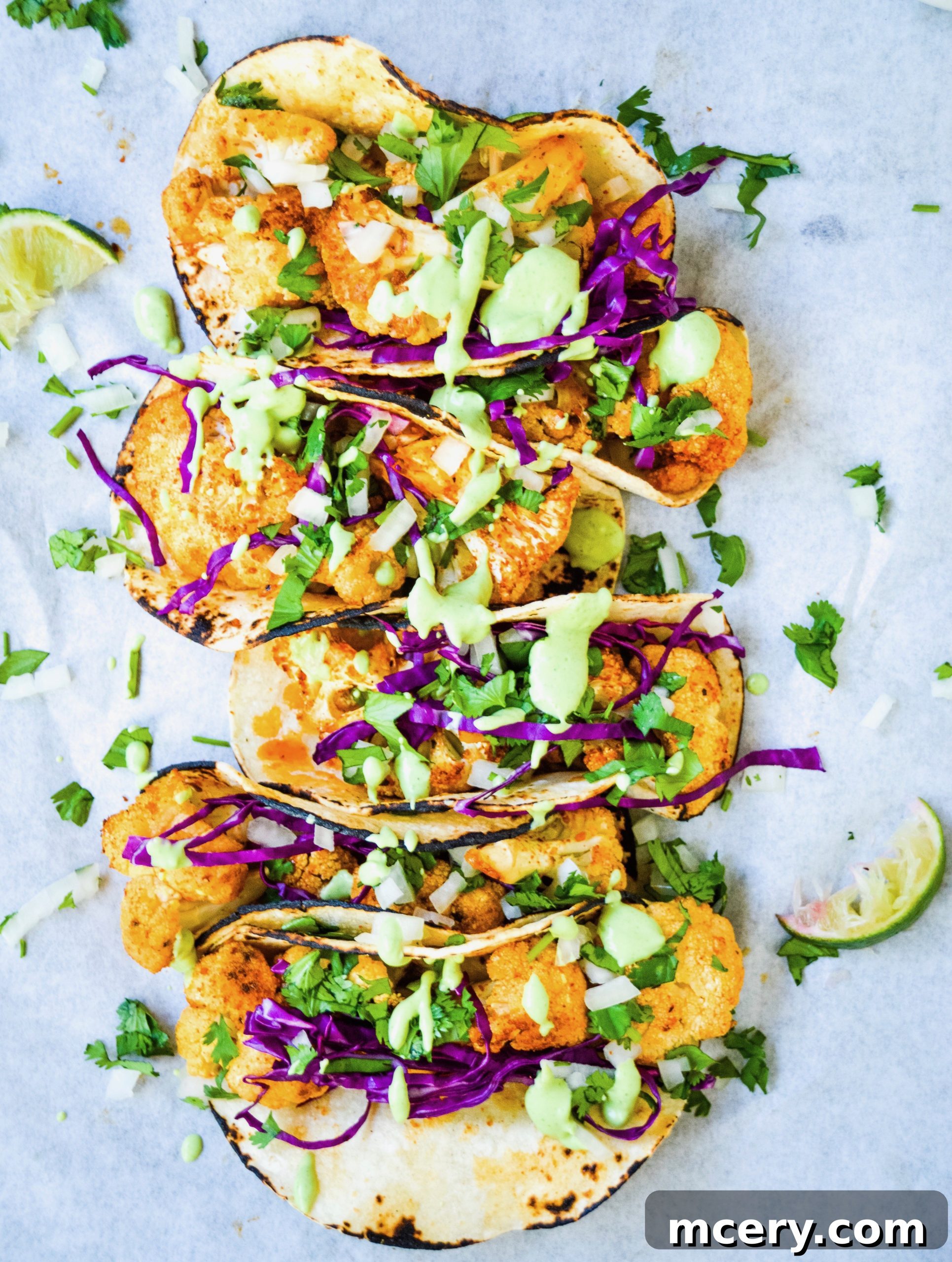 Plateful of vibrant Roasted Cauliflower Tacos topped with fresh cilantro, onions, and a generous drizzle of tangy green crema, with lime wedges on the side.