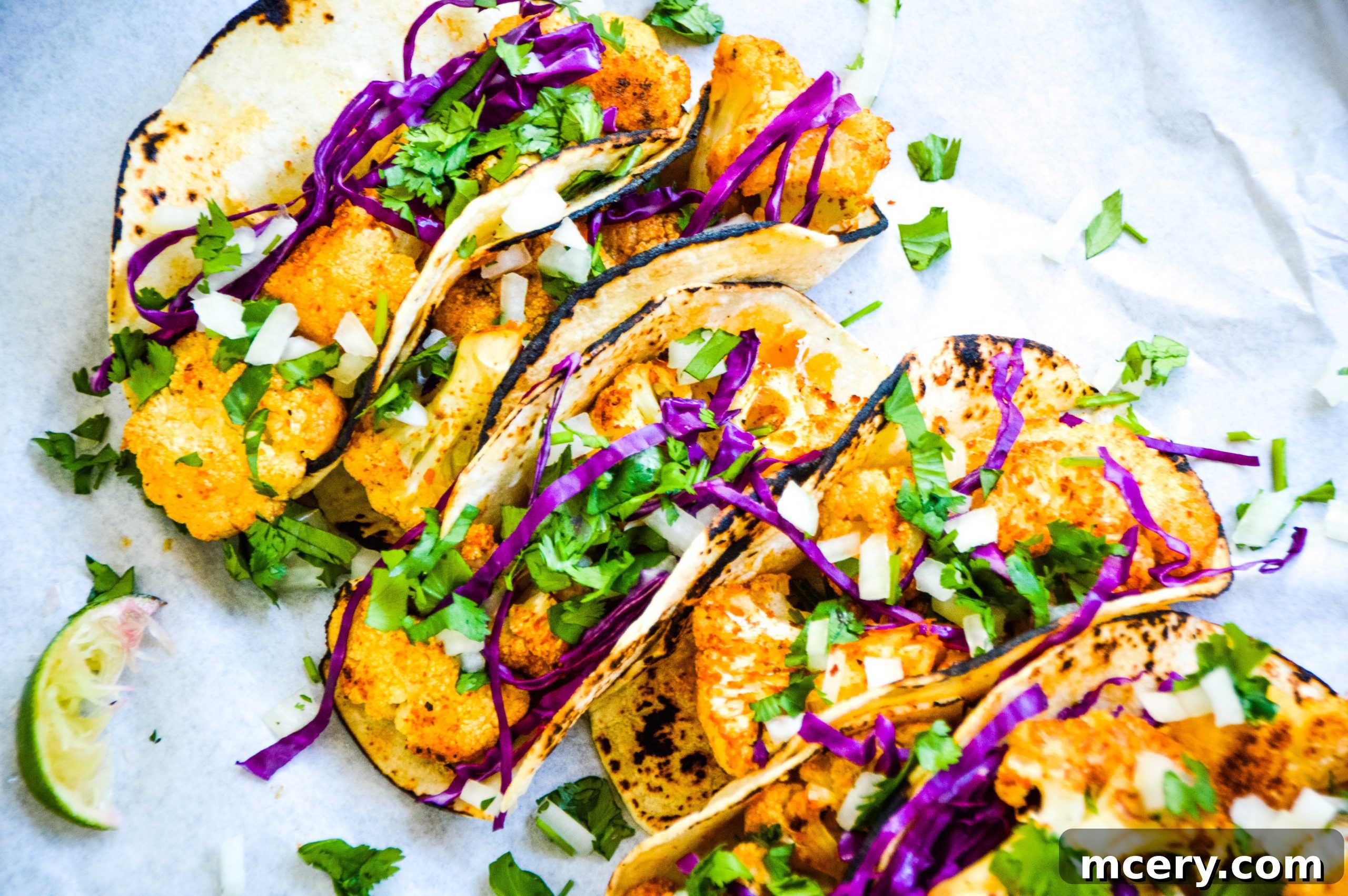 Roasted cauliflower florets seasoned with taco spices, spread evenly on a large baking sheet, ready for the oven.