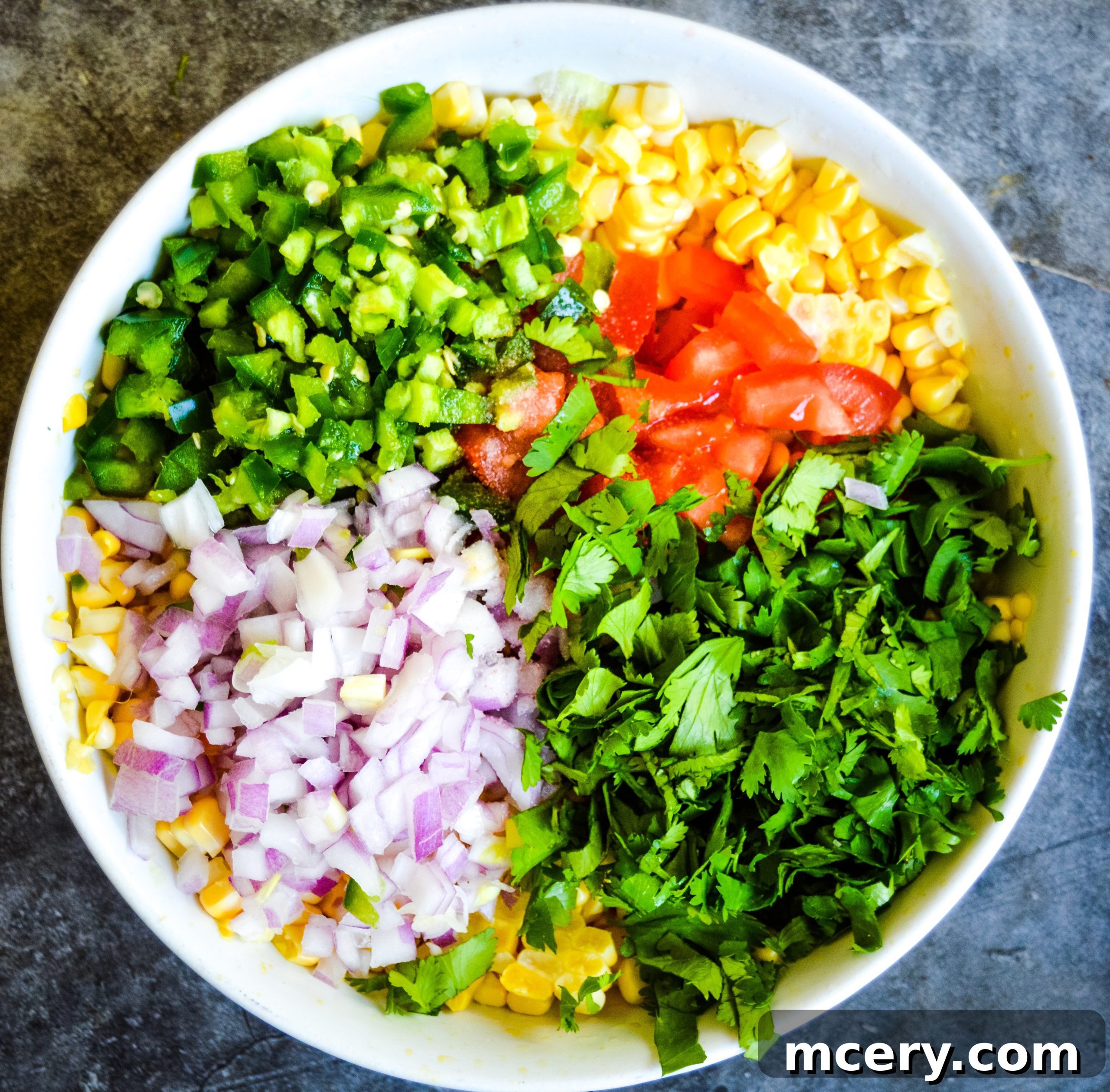Sunshine Corn Salsa 4 A bowl of homemade corn salsa surrounded by fresh ingredients like corn cobs, limes, and cilantro.