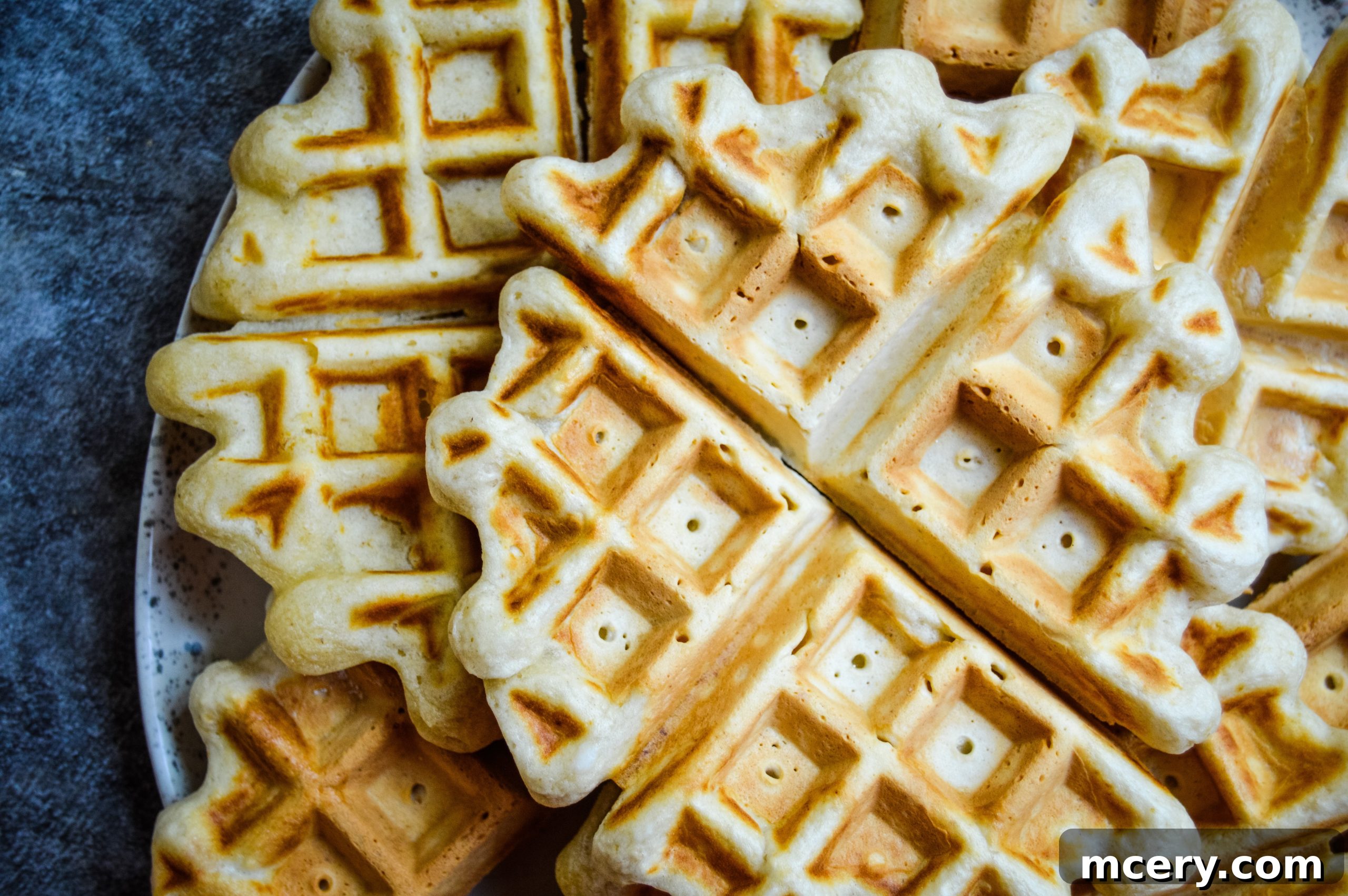 Close-up of a golden waffle piece with a generous spoon of fresh strawberry sauce being added.