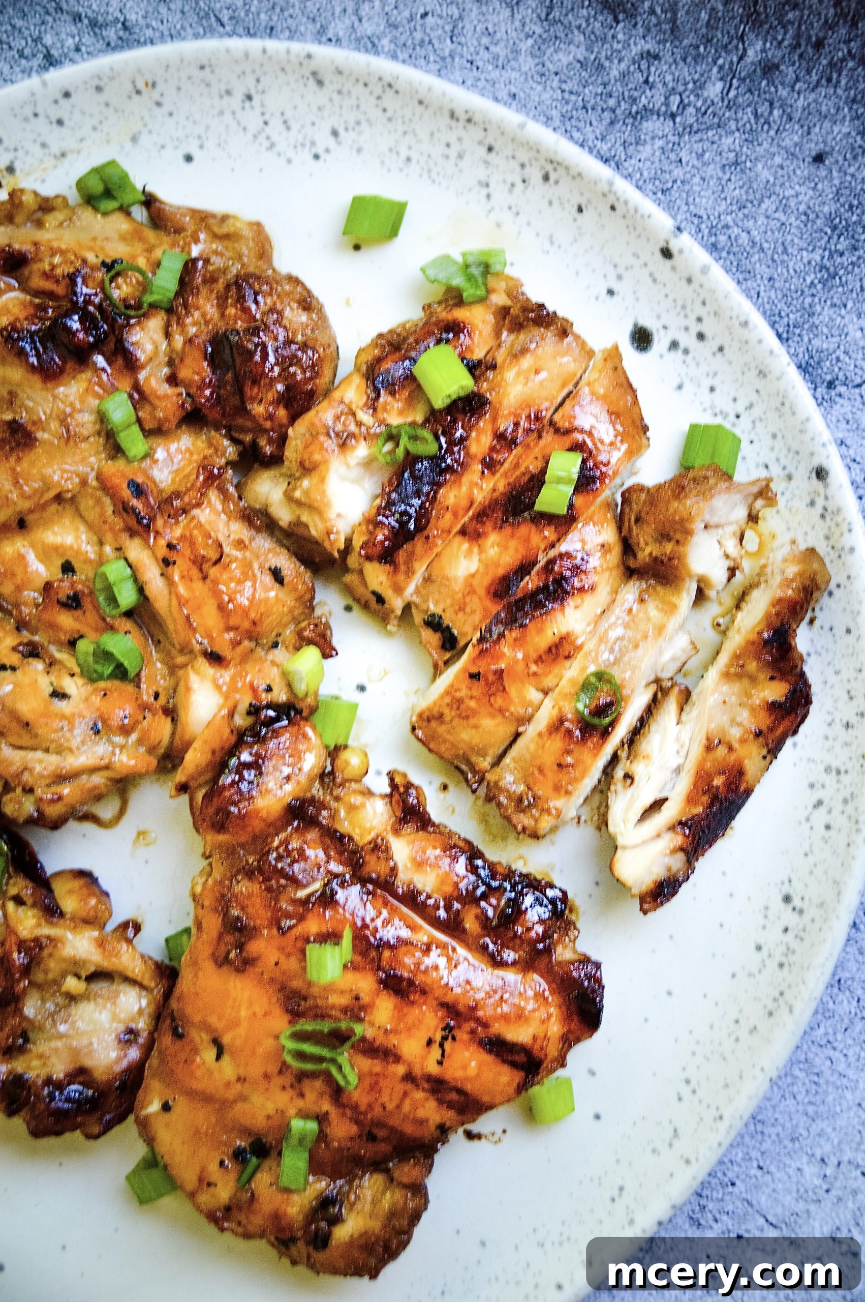 A close-up shot of grilled teriyaki chicken, topped with sesame seeds and chopped green onions, ready to be served.