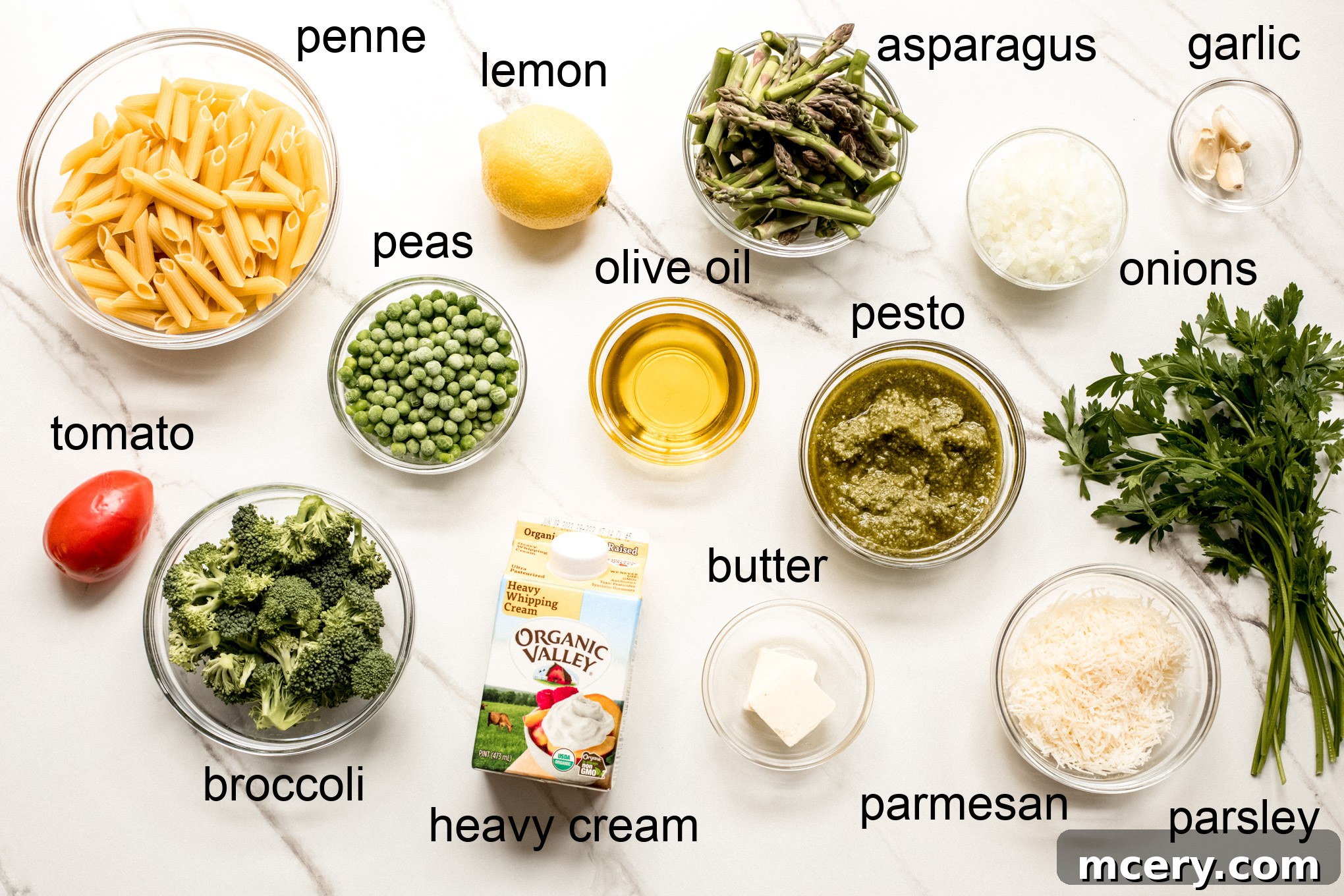 An overhead shot showcasing a vibrant collection of fresh ingredients laid out on a kitchen counter, including penne pasta, various green vegetables, tomatoes, and herbs, all prepared for making Penne Primavera.