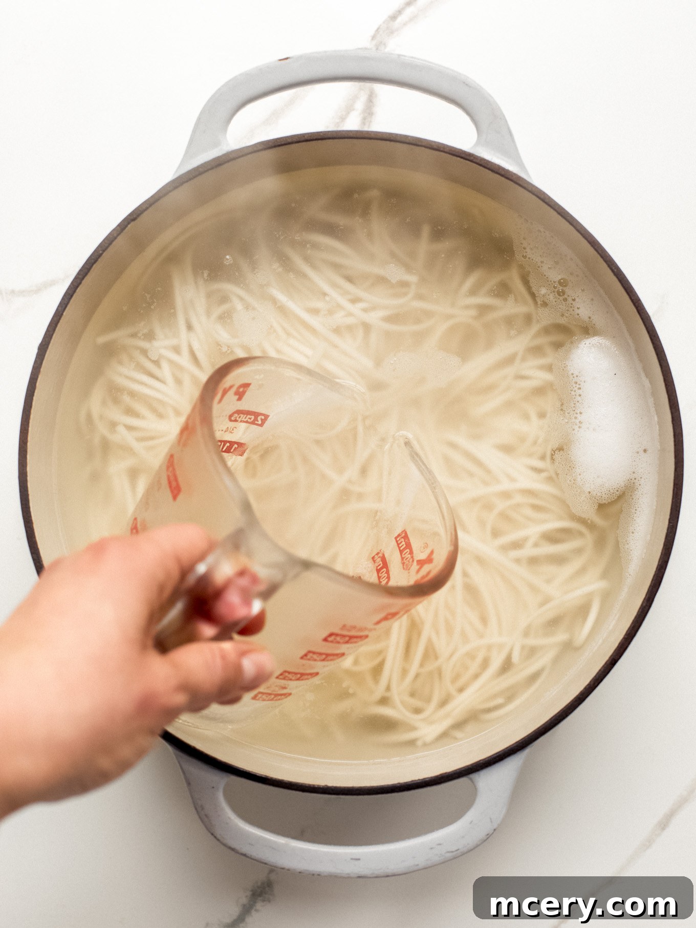 Irresistible Creamy Cajun Sausage Pasta 4 pasta in a pot with reserve pasta water in a measuring cup on the side.