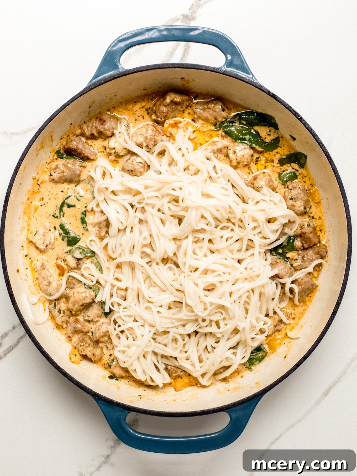 Irresistible Creamy Cajun Sausage Pasta 8 cooked pasta over sausage in cream sauce in saute pan.