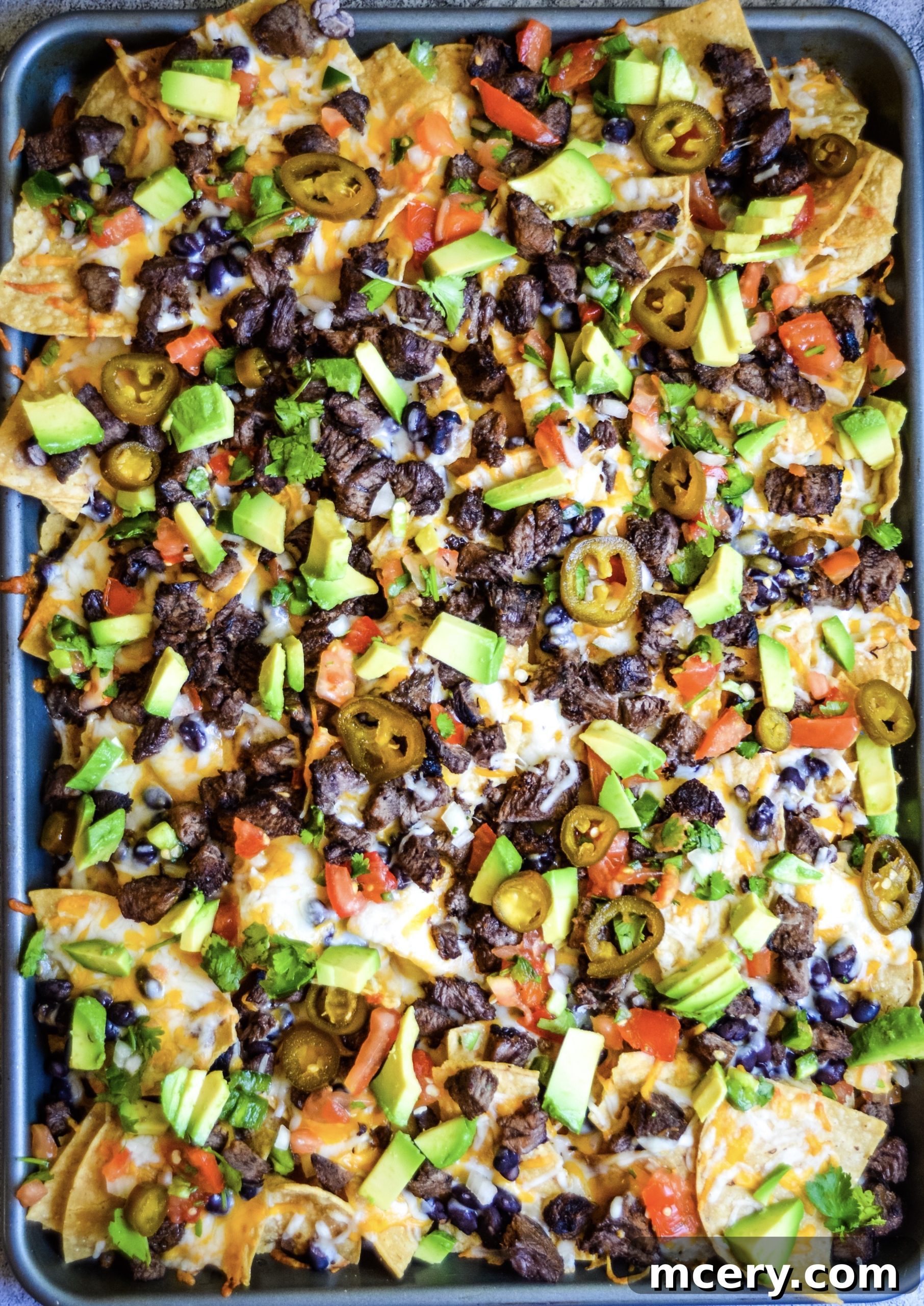 Loaded Carne Asada Nachos 2 A generous plate of freshly made Carne Asada Nachos, featuring a base of crispy tortilla chips loaded with melted cheese, succulent grilled steak, black beans, and diced toppings.