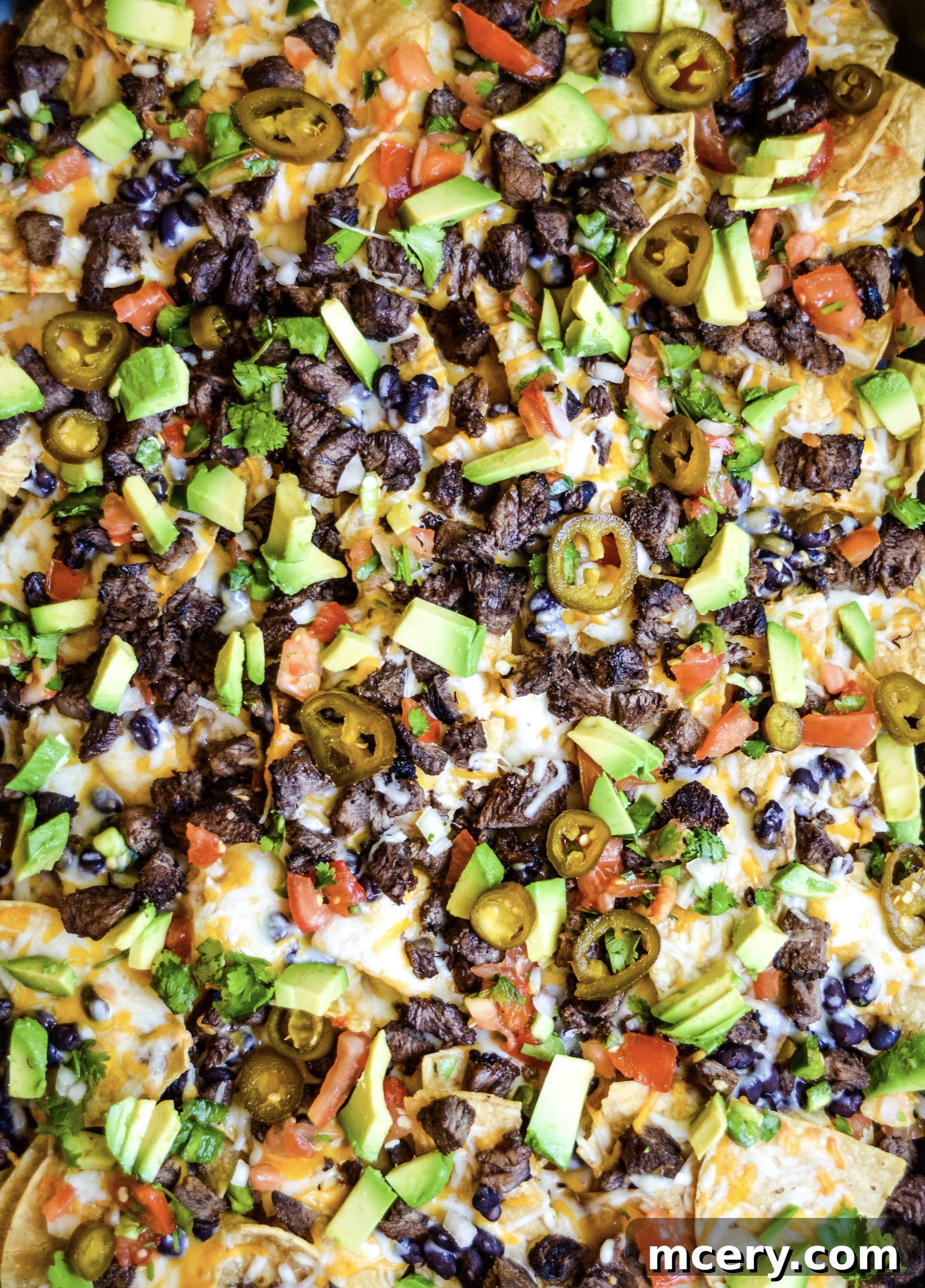 Loaded Carne Asada Nachos 4 A close-up shot of baked Carne Asada Nachos, showing melted cheese bubbling over the chips, steak, and beans, just before the fresh toppings are added.
