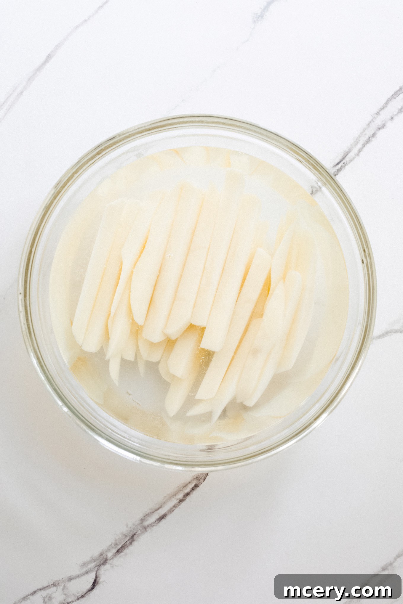 Signature Old Bay Fries 5 sliced potatoes in a bowl covered by water.