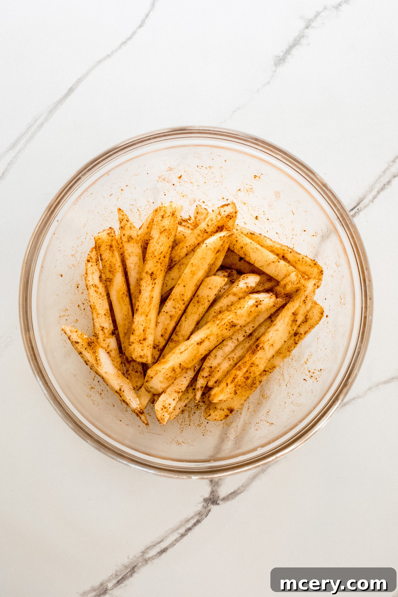 Signature Old Bay Fries 8 potatoes in a glass bowl tossed with oil and spices.
