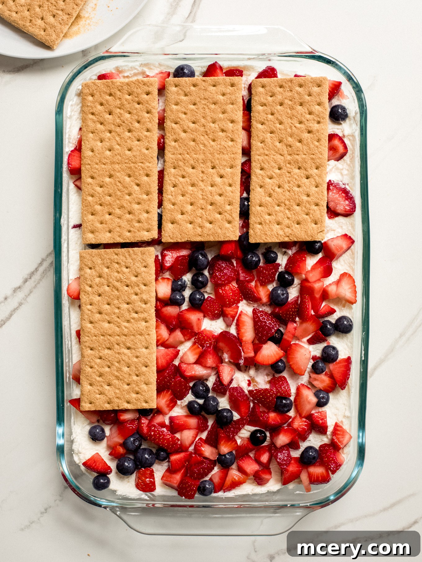 Another layer of graham crackers neatly placed over the fruit layer in the glass dish, creating the next structural component of the icebox cake.