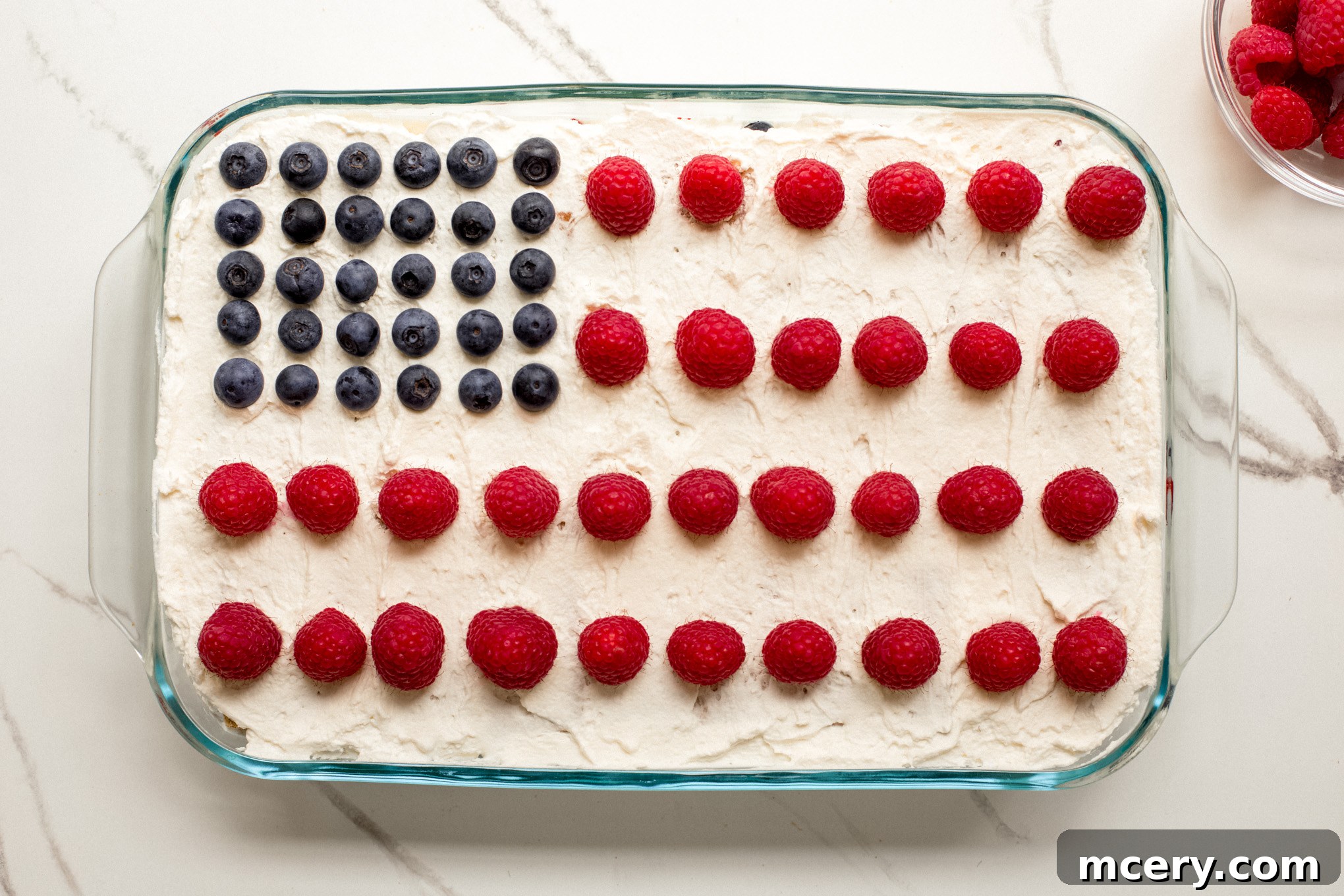 The fully assembled icebox cake in a glass dish, meticulously decorated with blueberries forming the 'stars' and raspberries creating the 'stripes' of the American flag.
