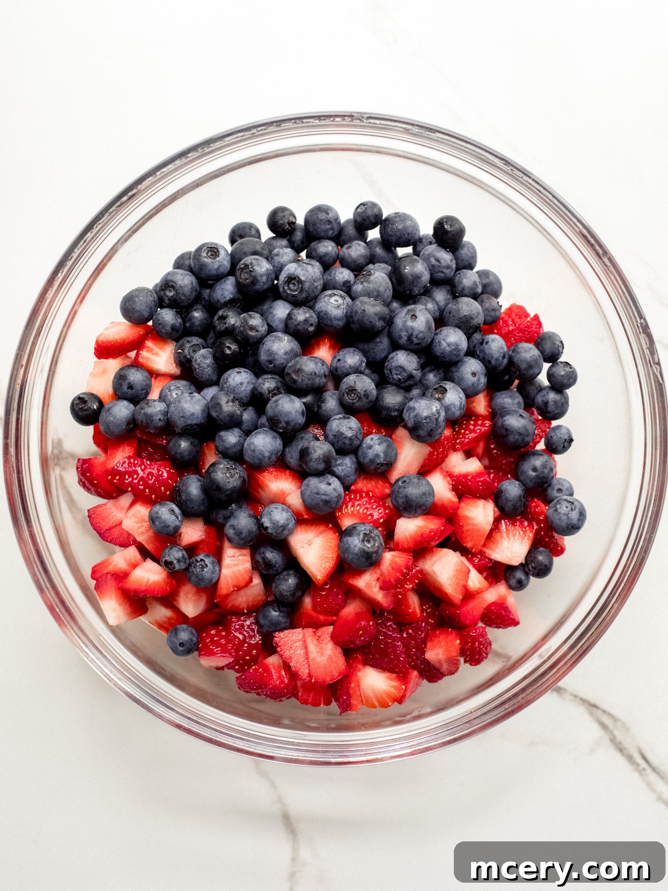A glass bowl filled with freshly chopped strawberries and vibrant blueberries, ready to be mixed for the icebox cake.