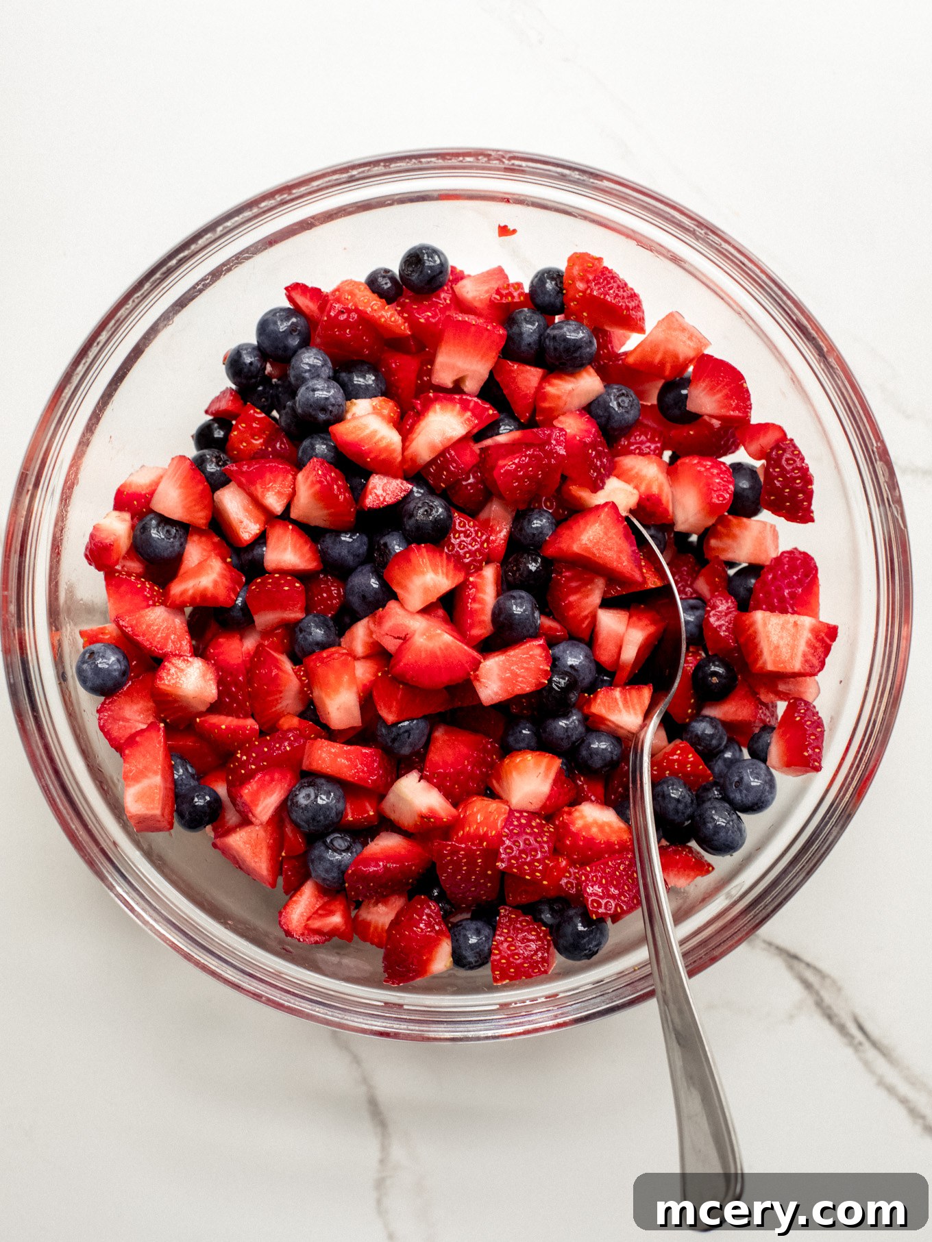 A closer view of the mixed chopped strawberries and blueberries in a glass bowl, showcasing their vibrant colors and readiness for the cake layers.