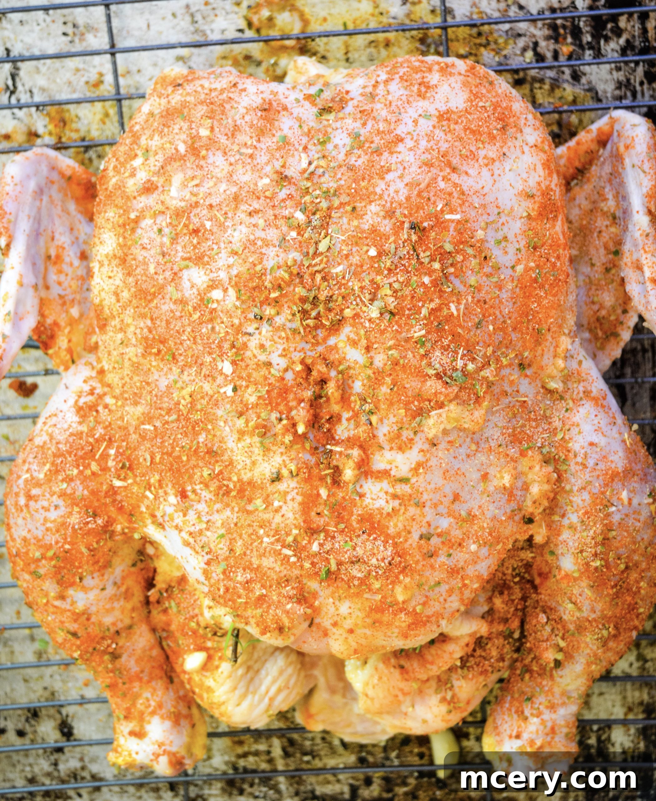 Raw whole chicken prepared for roasting, stuffed with lemon and herbs, resting on a bed of chopped potatoes and squash in a large pot.