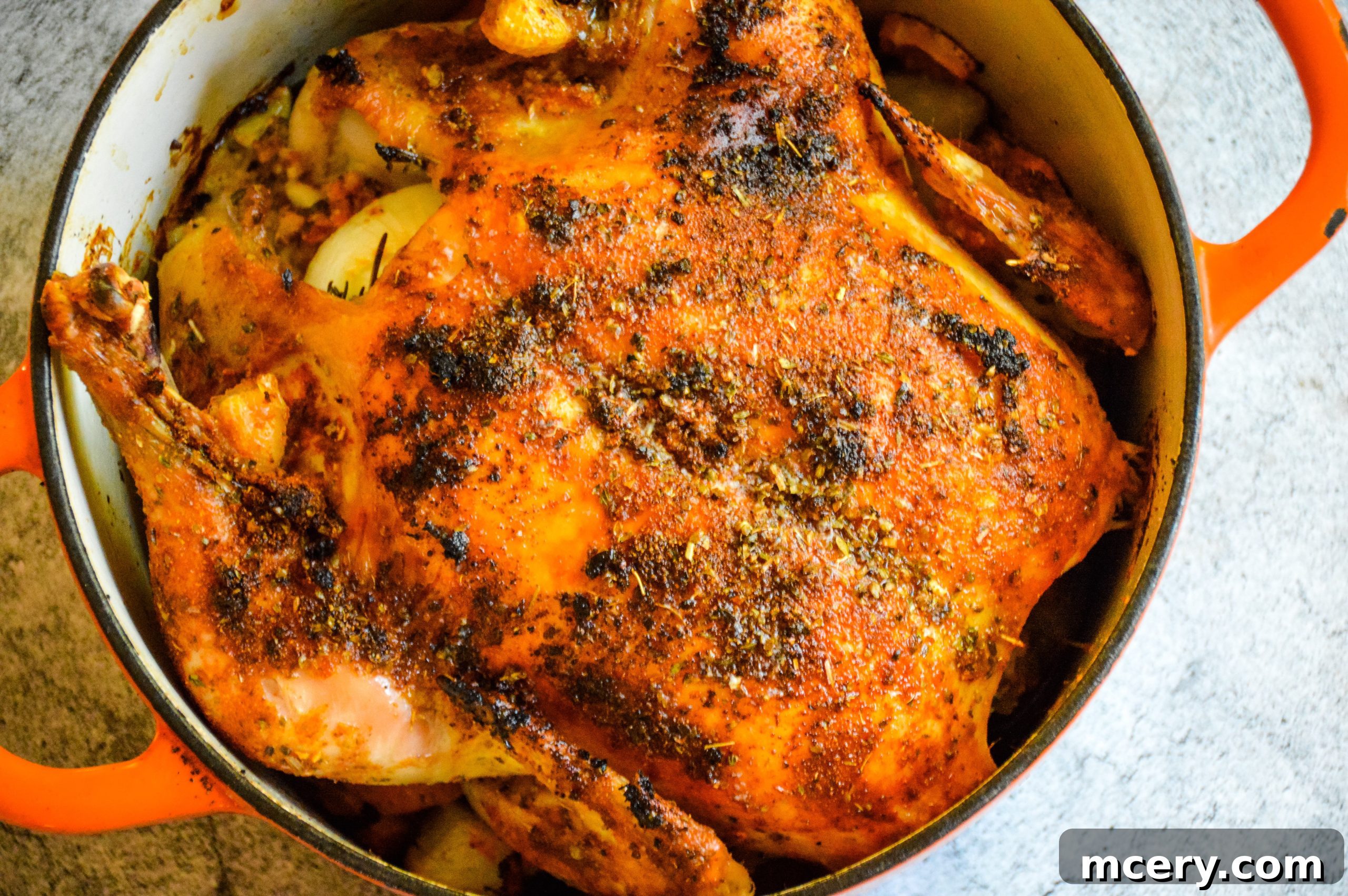 A whole roasted chicken, just out of the oven, covered in a golden-brown, crispy skin, surrounded by roasted vegetables.
