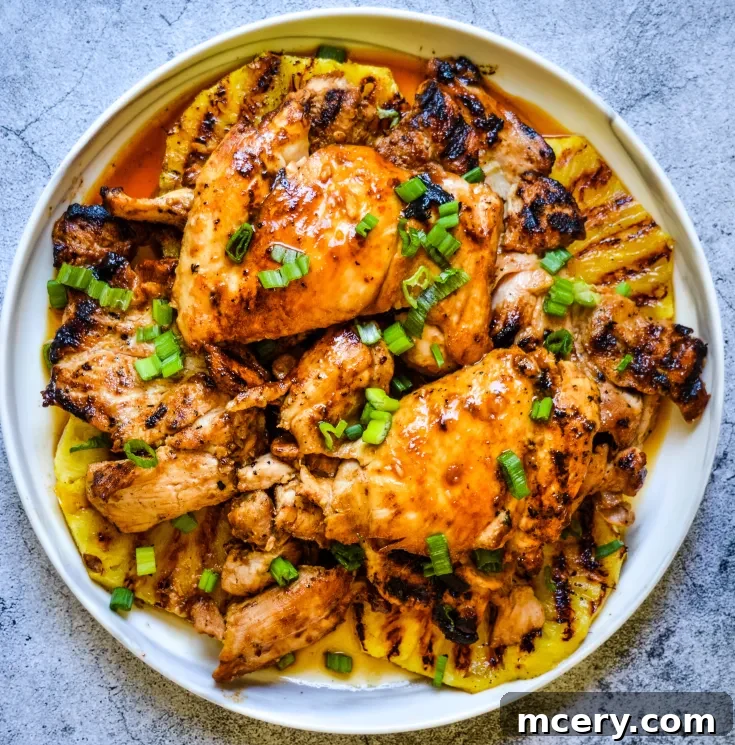 Grilled Huli Huli Chicken with char marks are topped with chopped green onions and arranged on a plate. Juicy and golden, the chicken is served with pieces of grilled pineapple.