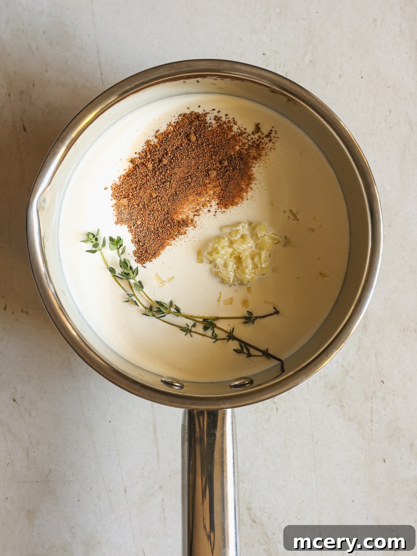 Heavy cream infused with fresh spices, garlic, and thyme in a small saucepan.