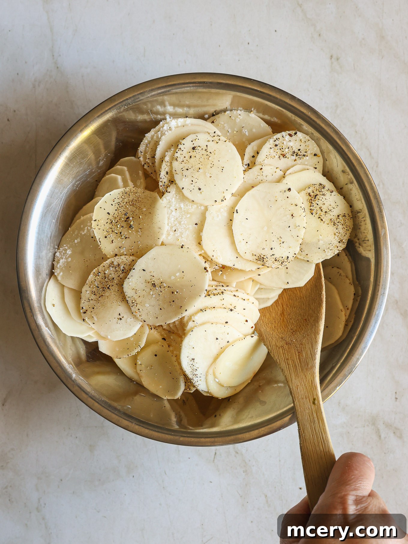 Thinly sliced potatoes in a bowl, seasoned with salt and pepper.