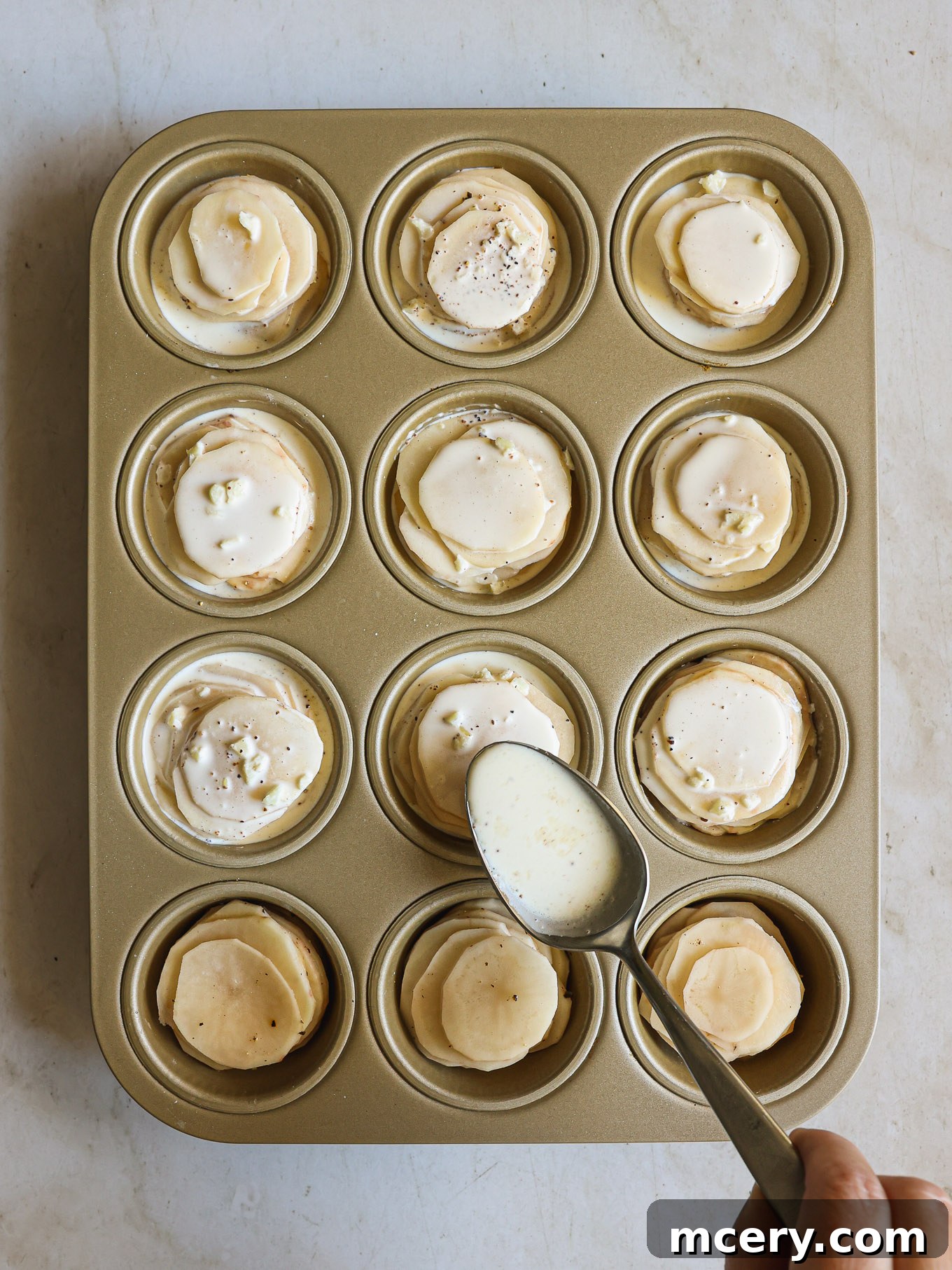 Individual potato stacks arranged in a muffin pan with cream poured over them.