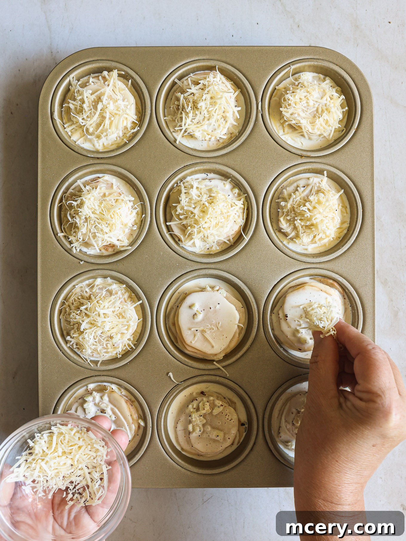 Potato stacks in a muffin pan, generously topped with Parmesan cheese, ready for baking.