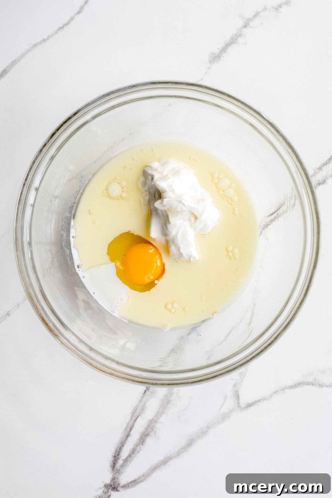 Golden Pear Cake 4 Wet ingredients including egg, oil, and sour cream being whisked together in a clear glass mixing bowl.