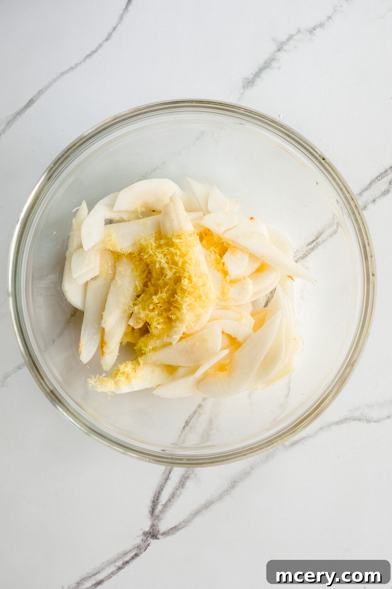Golden Pear Cake 8 Finely sliced pears tossed with lemon zest and lemon juice in a bowl, preparing for topping.