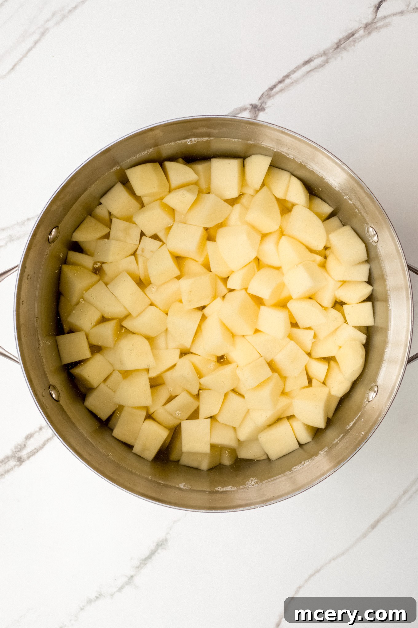 Silky Yukon Gold Mash 4 Cut up Yukon Gold potatoes submerged in cold water inside a large stockpot.