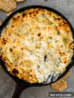 Baked artichoke dip in a cast iron skillet, garnished with fresh herbs.