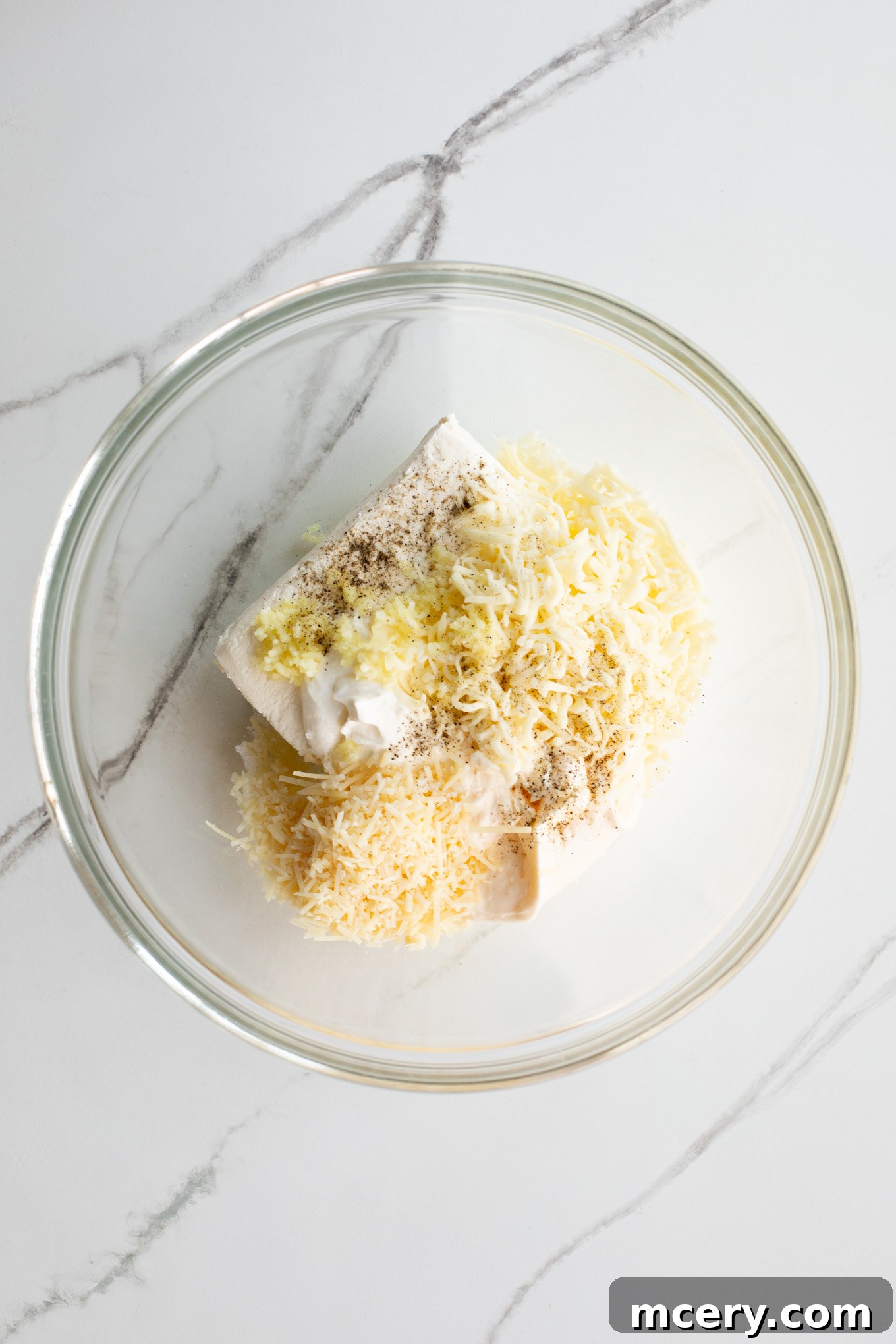 Spicy Jalapeno Artichoke Dip 4 Sour cream, mayonnaise, cream cheese, and shredded cheeses are combined in a large glass mixing bowl.