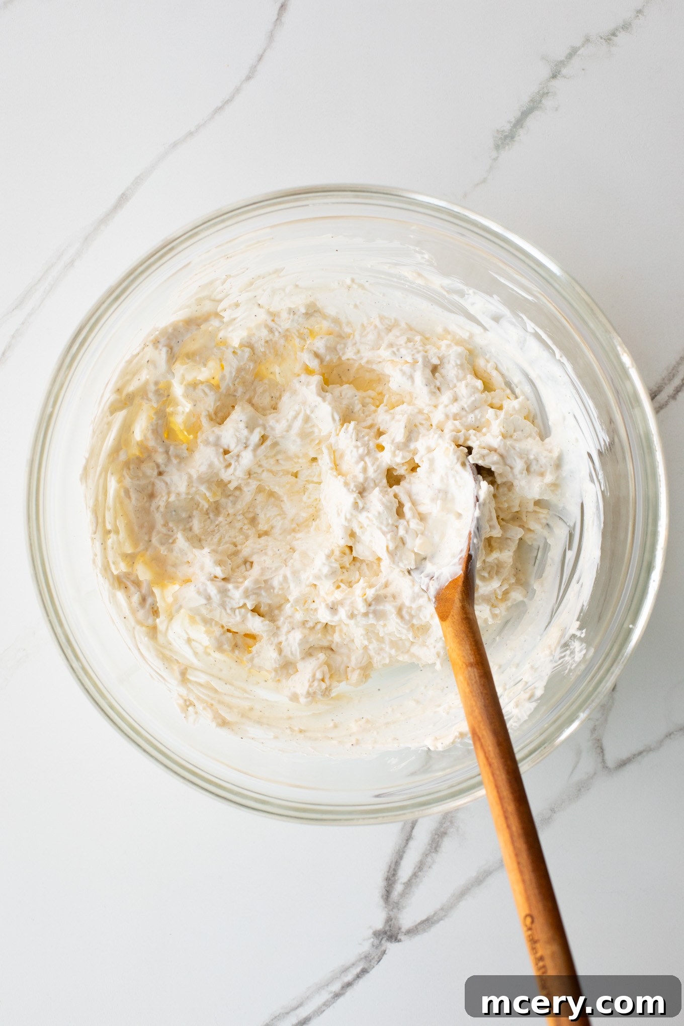 Spicy Jalapeno Artichoke Dip 5 The creamy mixture of cheeses, sour cream, and mayonnaise has been thoroughly mixed until smooth in a glass bowl.