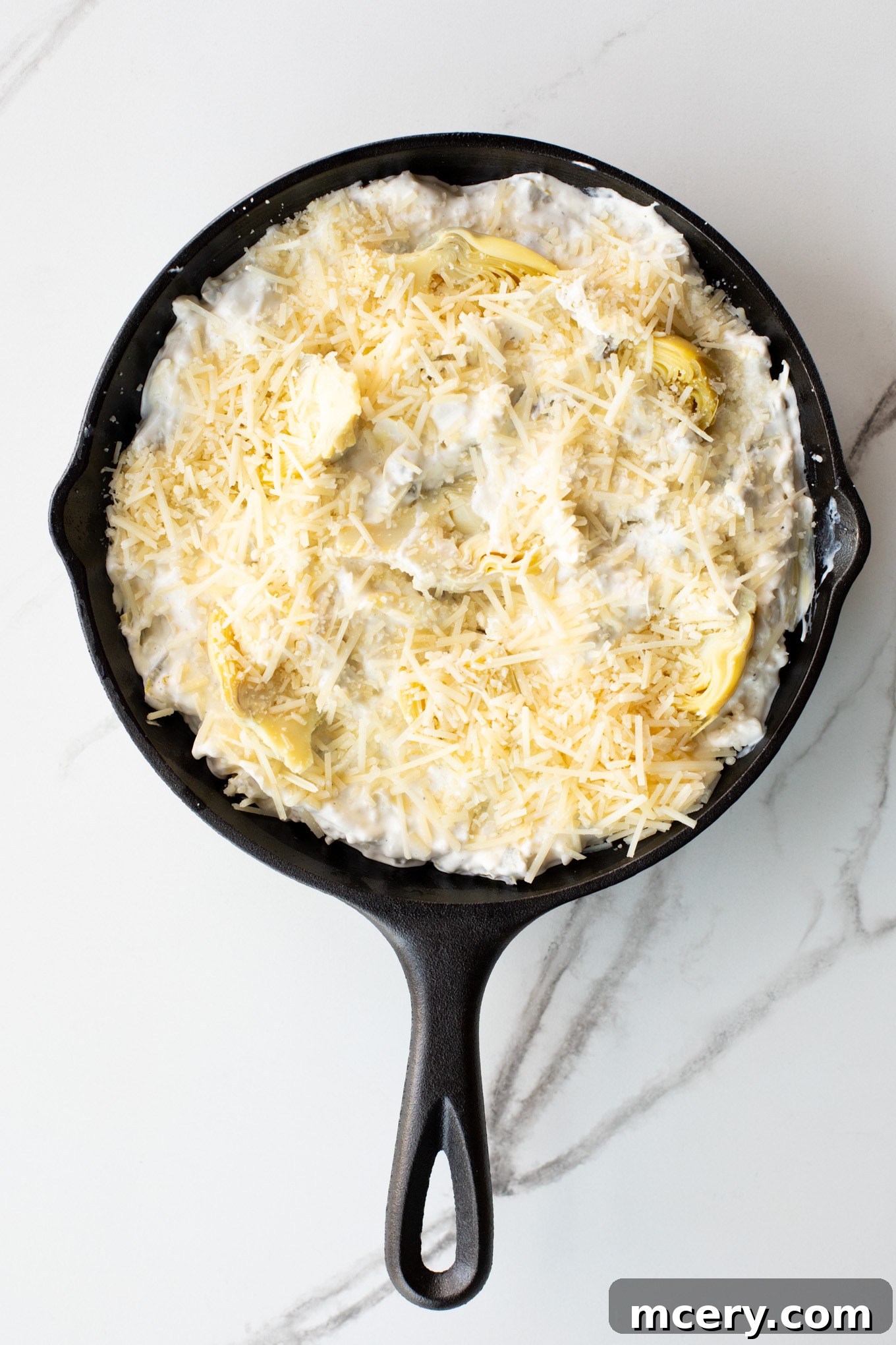 Spicy Jalapeno Artichoke Dip 7 The jalapeno artichoke dip mixture is spread into a cast iron skillet and topped with additional cheese before baking.