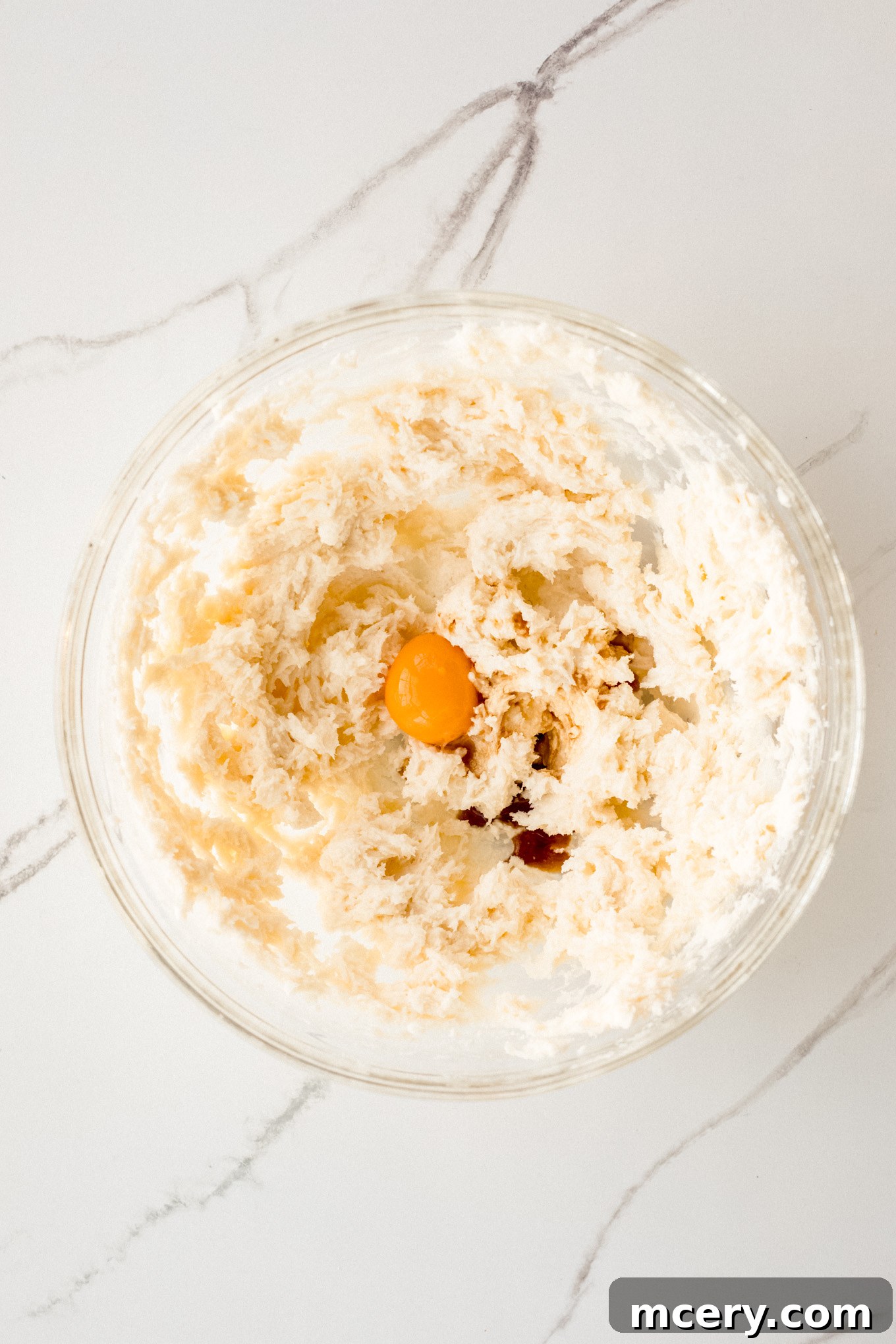 Buttery Pecan Snowflakes 5 A smooth, whipped mixture of butter, sugar, and egg yolk in a glass mixing bowl, showcasing the creamy consistency before dry ingredients are added.