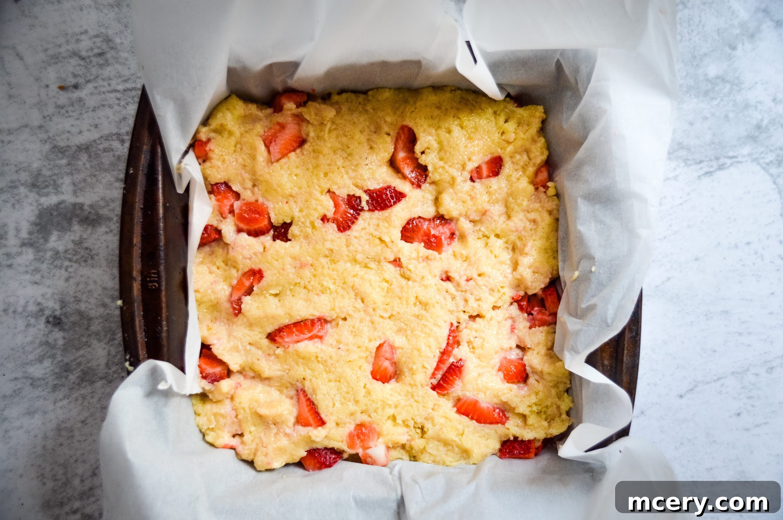 Strawberry Crumb Coffee Cake 7 Thick strawberry cake batter being pressed evenly into a square baking pan, ready for the streusel topping.