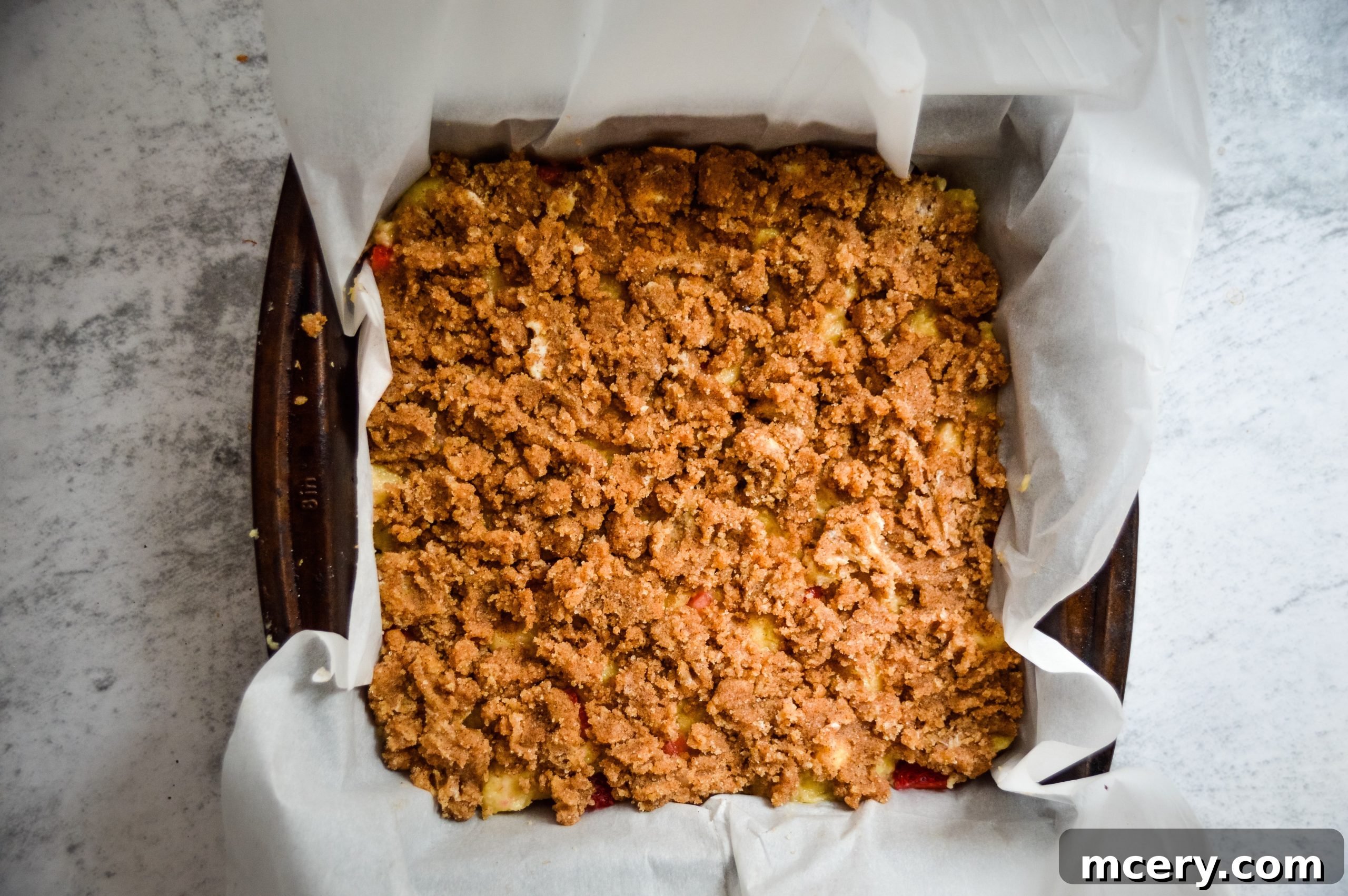 Strawberry Crumb Coffee Cake 9 The prepared streusel topping generously sprinkled over the raw strawberry coffee cake batter in a baking pan, ready for the oven.