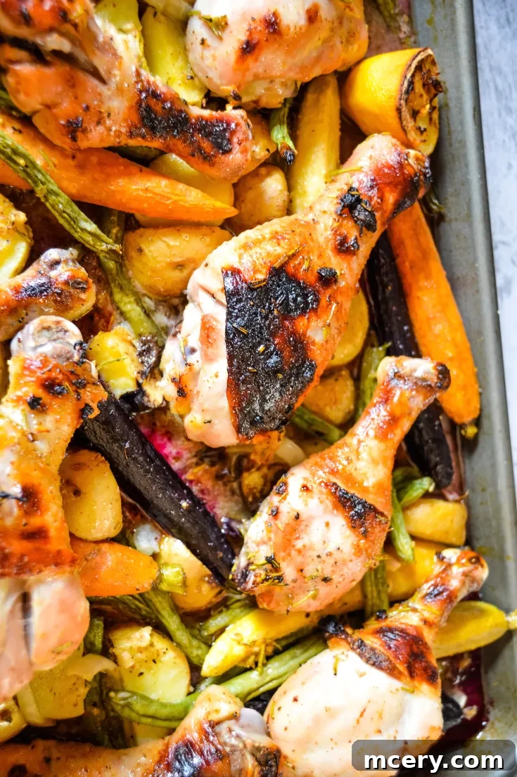 A baking sheet filled with roasted Garlic Herb Sheet Pan Chicken Drumsticks, assorted vegetables like carrots, potatoes, and green beans, garnished with fresh rosemary and lemon slices.