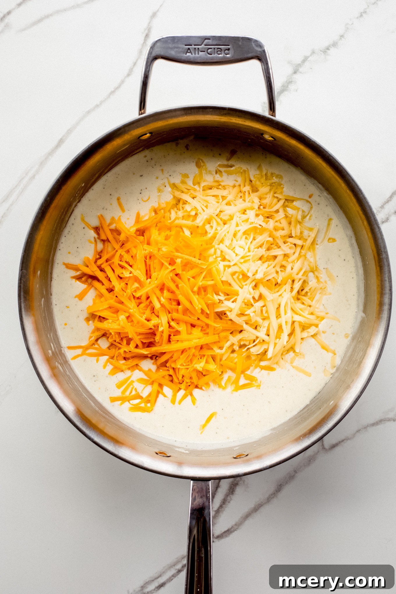 Velvet Smoked Gouda Mac 7 shredded cheese with milk mixture in a pan.