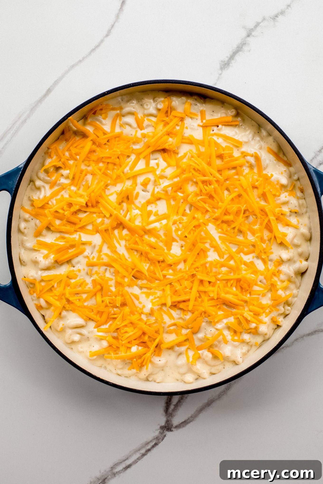 Velvet Smoked Gouda Mac 9 baked macaroni in a cast-iron skillet topped with shredded cheddar cheese.