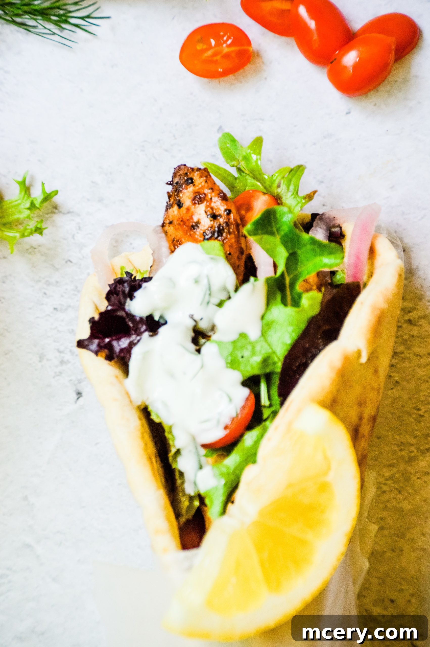 A beautifully assembled Greek Chicken Gyro, tightly wrapped in parchment paper, displaying the delicious filling.