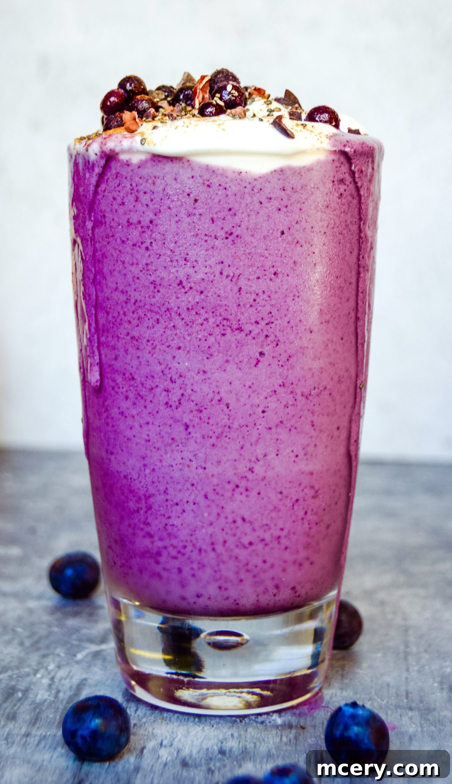 A glass of vibrant purple pregnancy blueberry smoothie, topped with fresh blueberries and a mint leaf, indicating a healthy and refreshing drink.