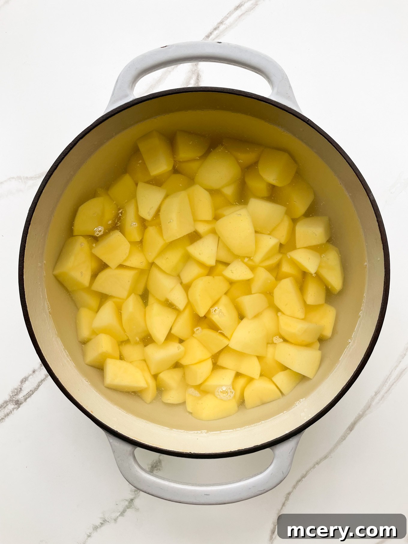 Peeled and cut potato chunks submerged in cold water within a large cooking pot, ready to be boiled.
