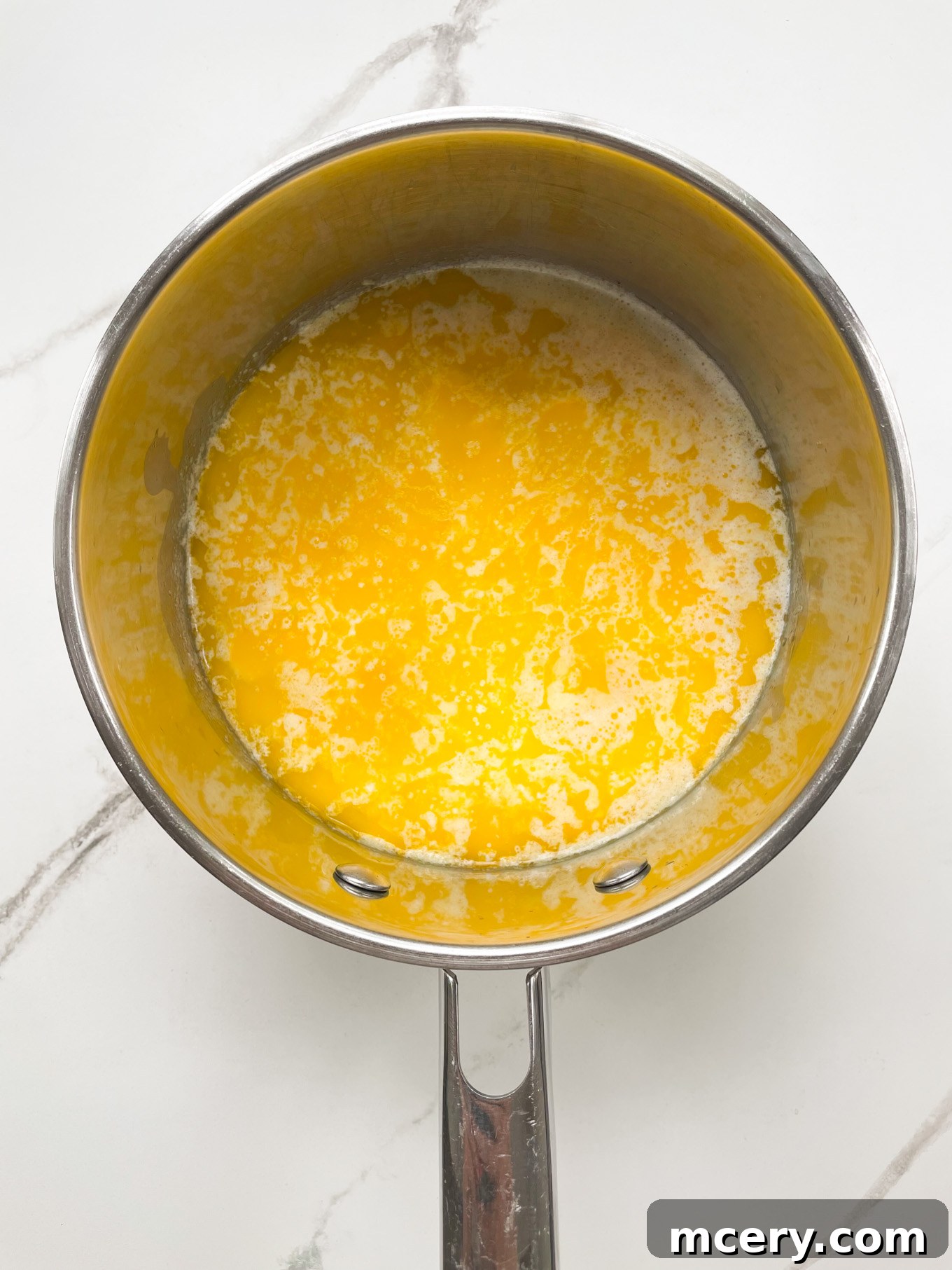 A small saucepan containing melted butter and milk, gently warmed on a stovetop, preparing to be added to the mashed potatoes.