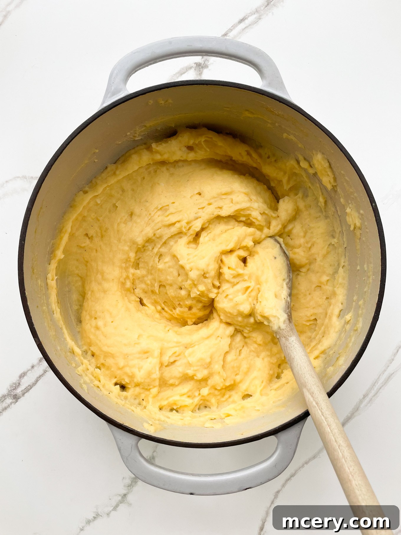 A large pot of creamy garlic mashed potatoes, perfectly mixed, with a wooden spoon resting inside, ready for final seasoning.