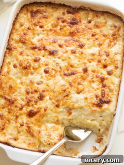 A generous serving of cheesy scalloped potatoes scooped out of a white casserole dish with a fork.