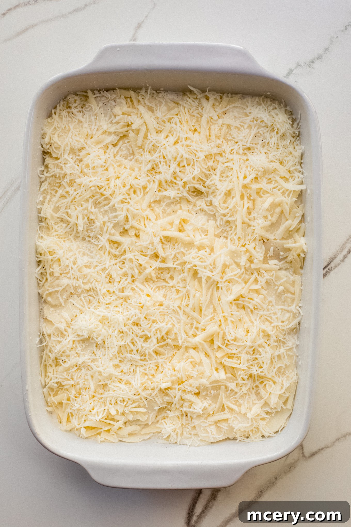 Decadent Cheesy Potato Gratin 7 A casserole dish with a layer of potatoes covered generously with shredded Gruyère and mozzarella cheese.