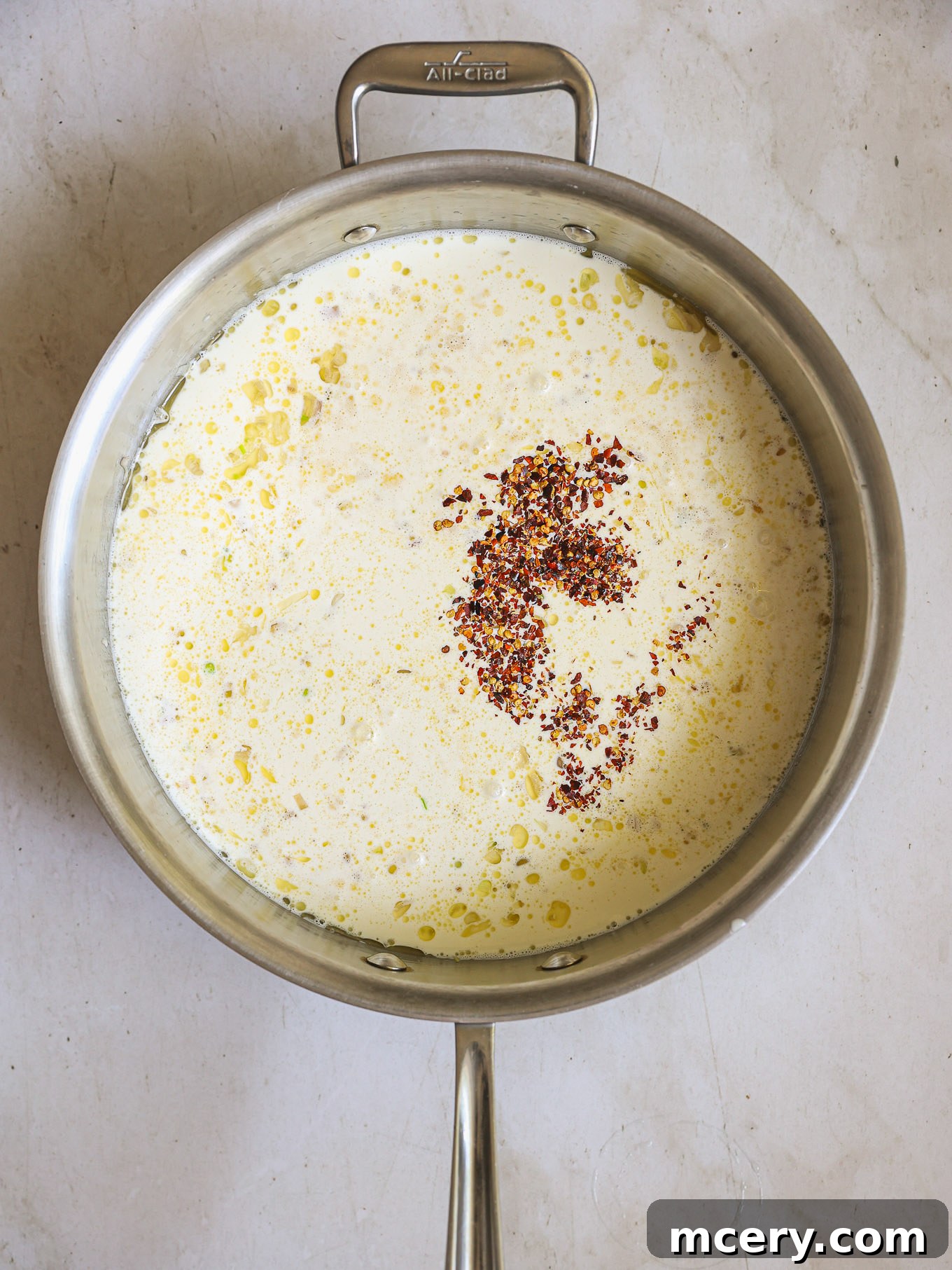 heavy cream, chicken broth, and red pepper flakes simmering in a pan.