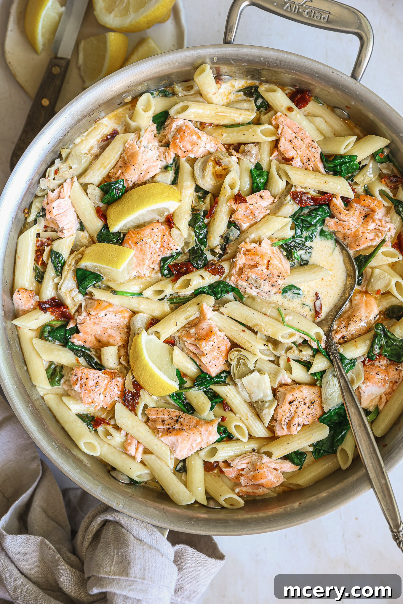 close-up of creamy salmon pasta with spinach and sun-dried tomatoes, garnished with fresh herbs.